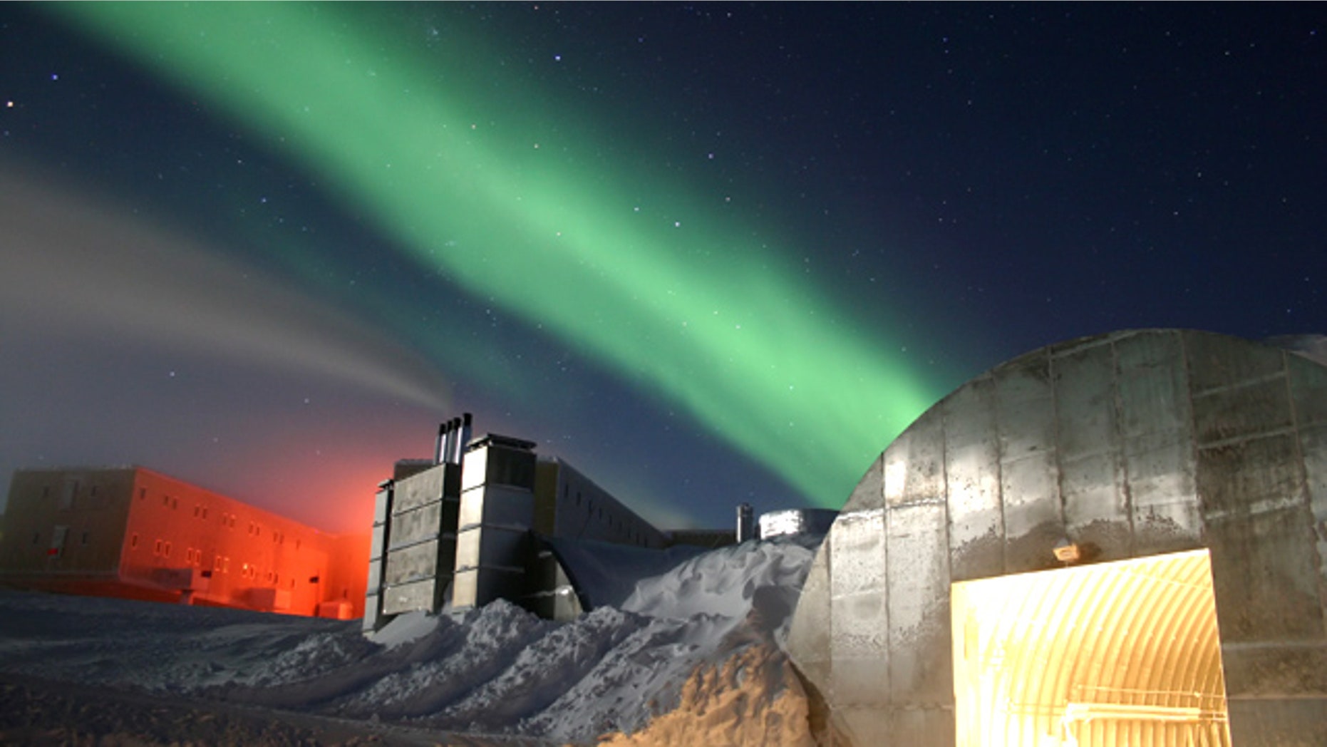 Amundsen-Scott South Pole Station during the long Antarctic night, with a new station at far left, power plant in the center and the Aurora Australis dancing through the sky.