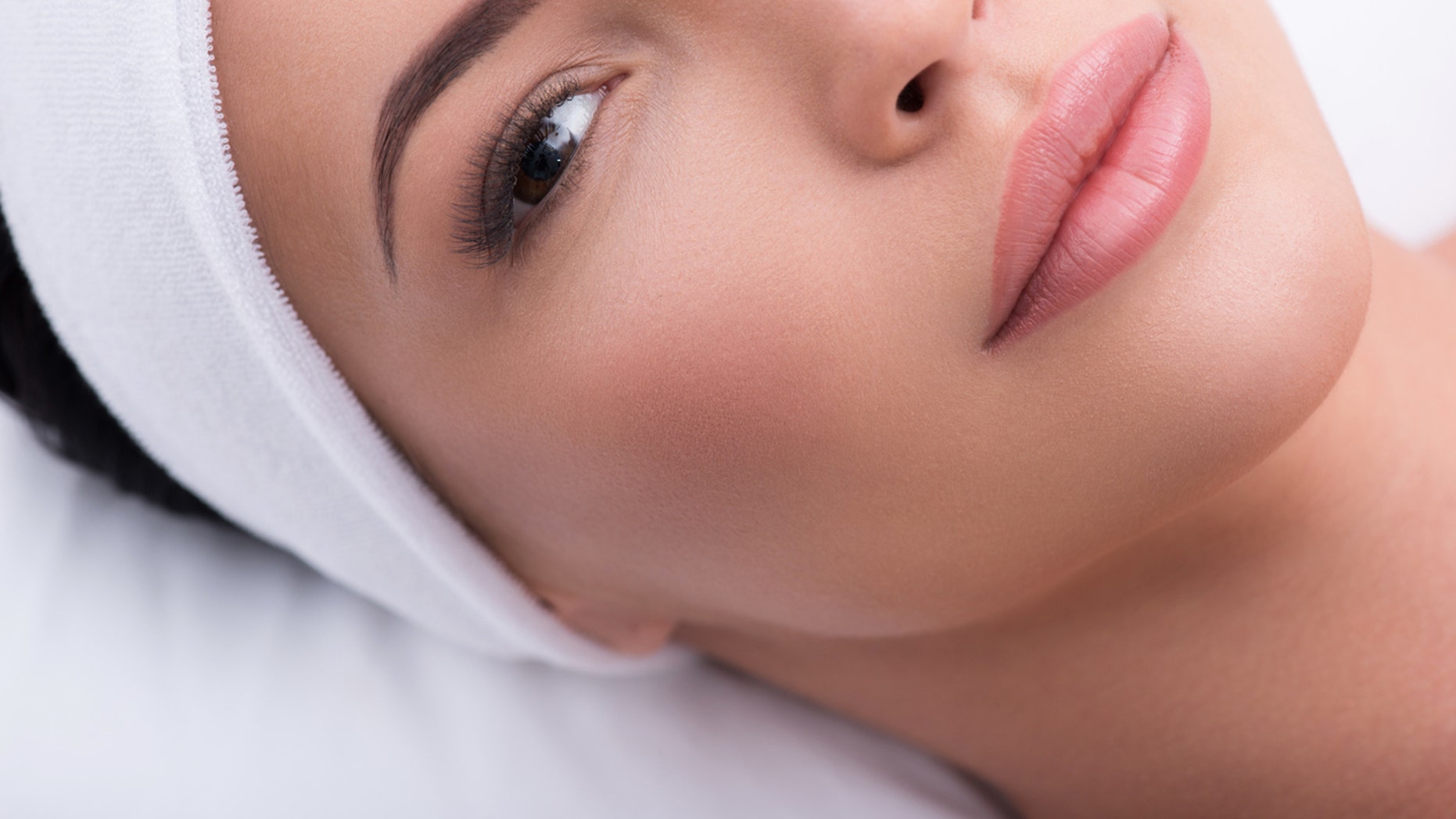 Top view close-up of beautiful woman with lengthened eyelashes. She is lying and looking at camera with confidence