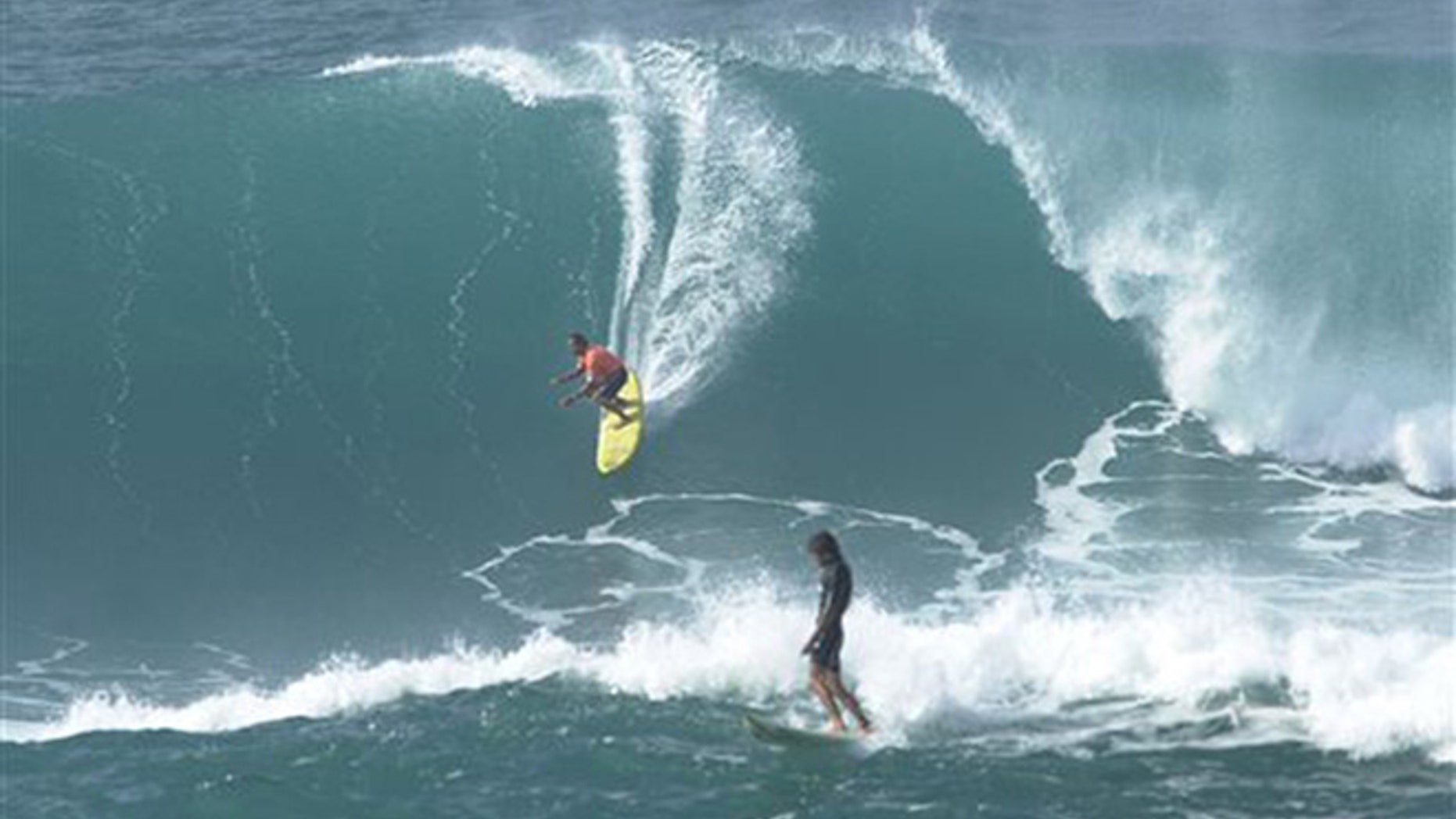 In this Jan. 7, 2002 file photo provided by World Surf League, Clyde Aikau, left, brother of Eddie Aikau, drops into a wave as Tony Ray, of Australia, finishes during the Quiksilver In Memory of Eddie Aikau big wave surf competition at Waimea Bay, Hawaii. (Ronen Zilbermen/World Surf League via AP, File)