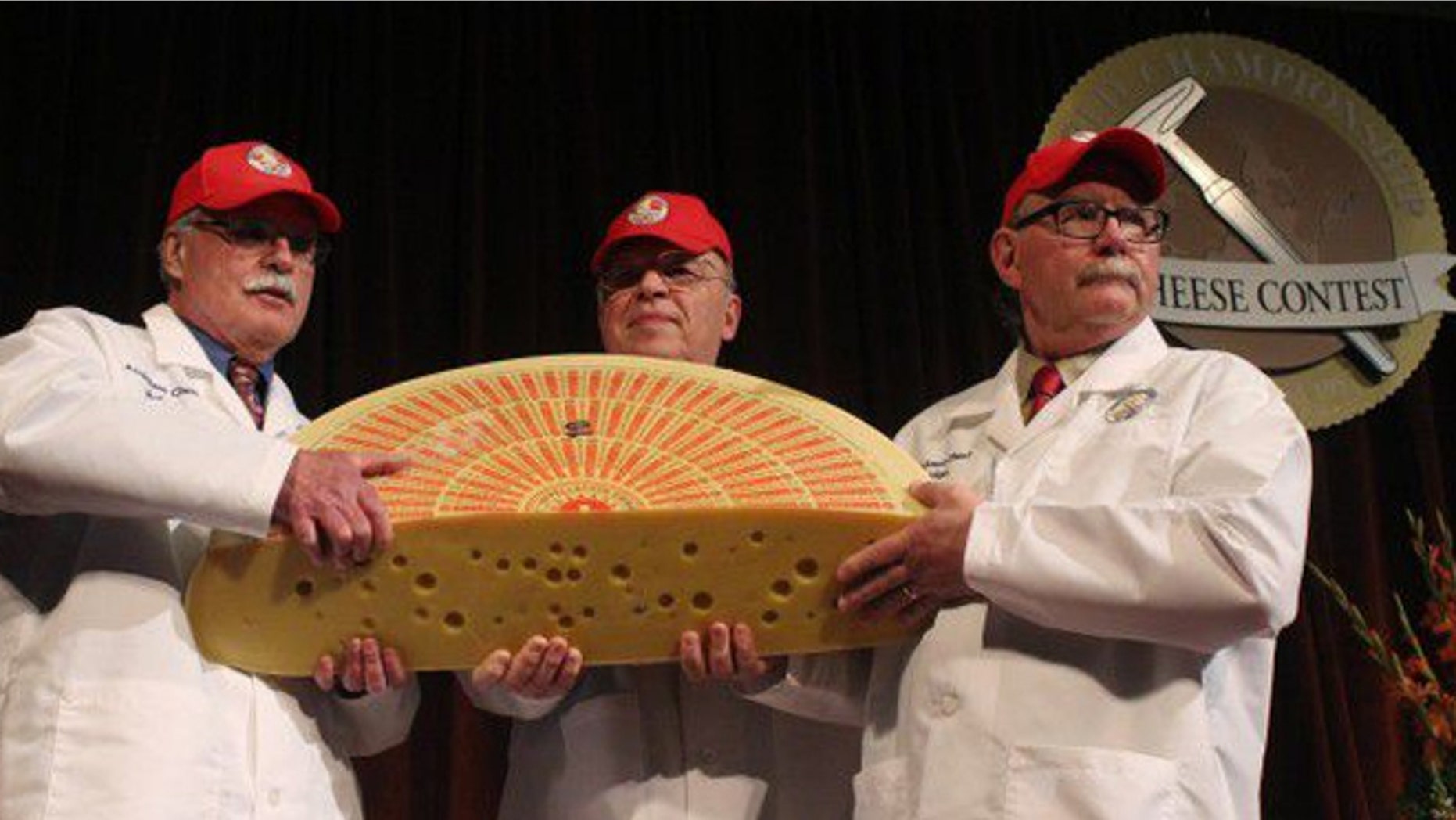 March 19, 2014: Three judges for the 2014 World Championship Cheese Contest hold the champion, a Swiss Emmentaler.