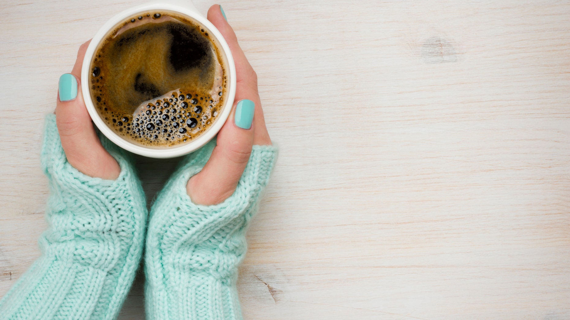 Female hands holding a coffee mug in knitted mittens