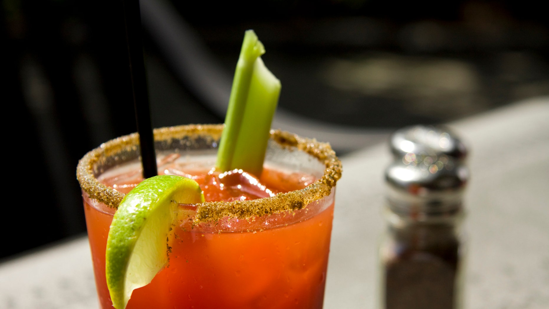 "Close up of a cool caesar or bloody mary cocktail drink rimmed with spice and garnished with lime wedge and celery stick. Shallow depth of field, good ad copy space."