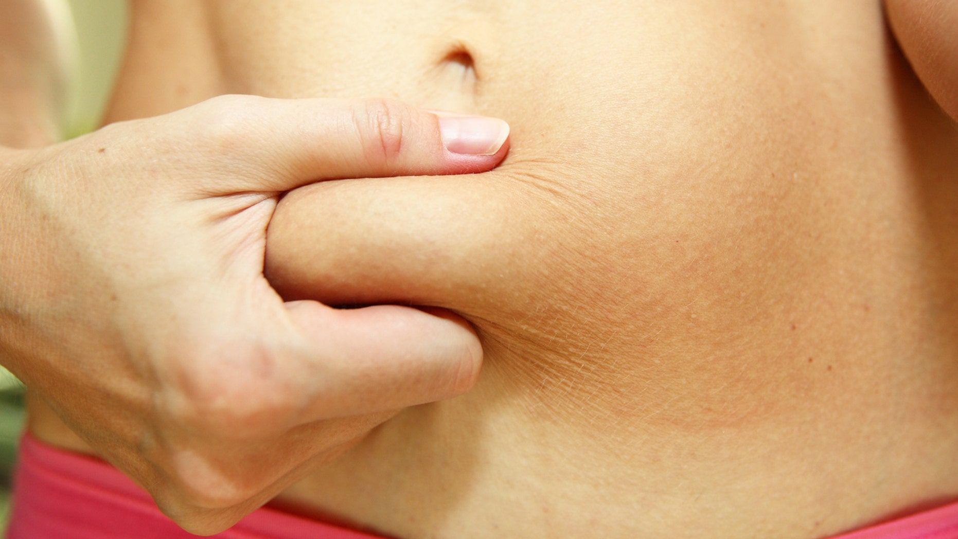 A close-up image of a slim young woman with a belly fat after giving birth. Woman's torso with some belly fat. Abdominal fat.