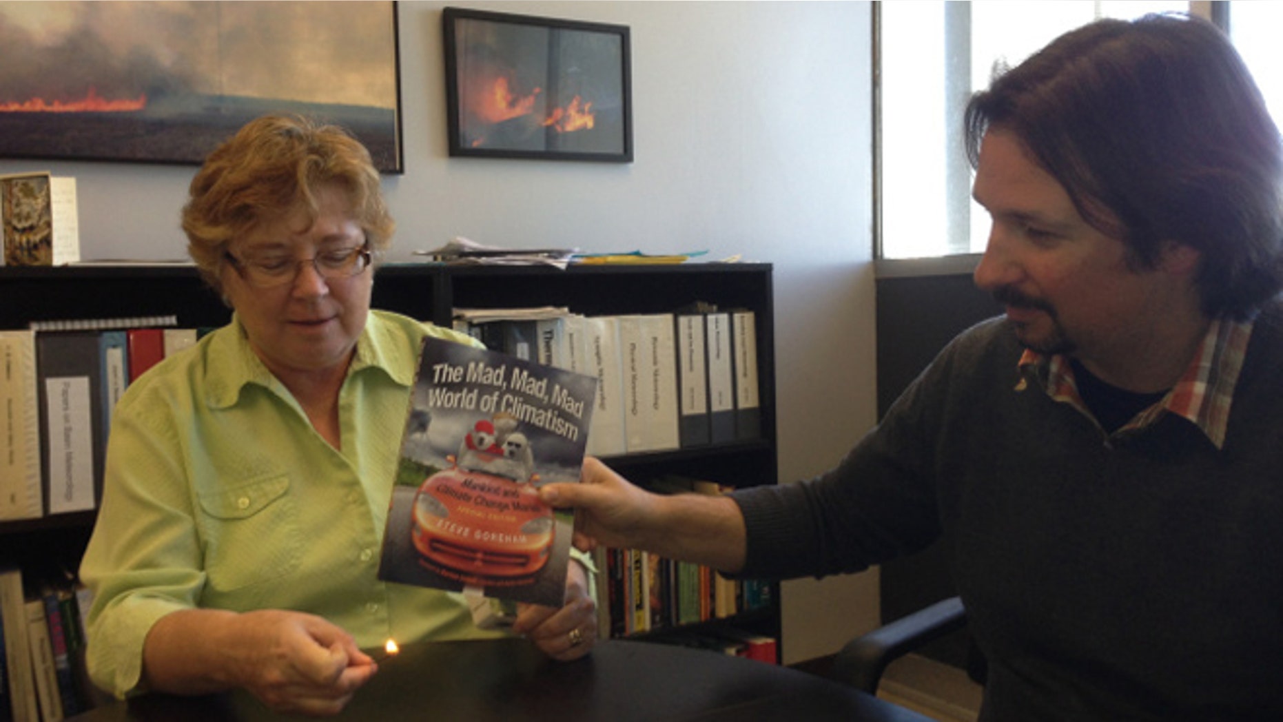 San Jose State University's Dr. Alison Bridger holds a lit match beneath a book that claims global warming is "natural" as assistant professor Craig Clements looks on last month. The photograph has since been removed from the university's website. (SJSU.edu)
