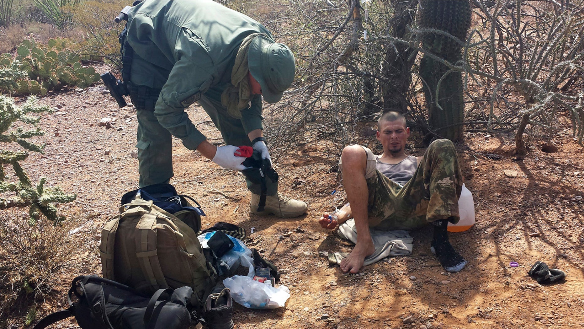 June 25, 2014: An unidentified U.S. Border Patrol agent, left, helps an immigrant, including setting up intravenous fluid replacement for dehydration, near Sells, Ariz.