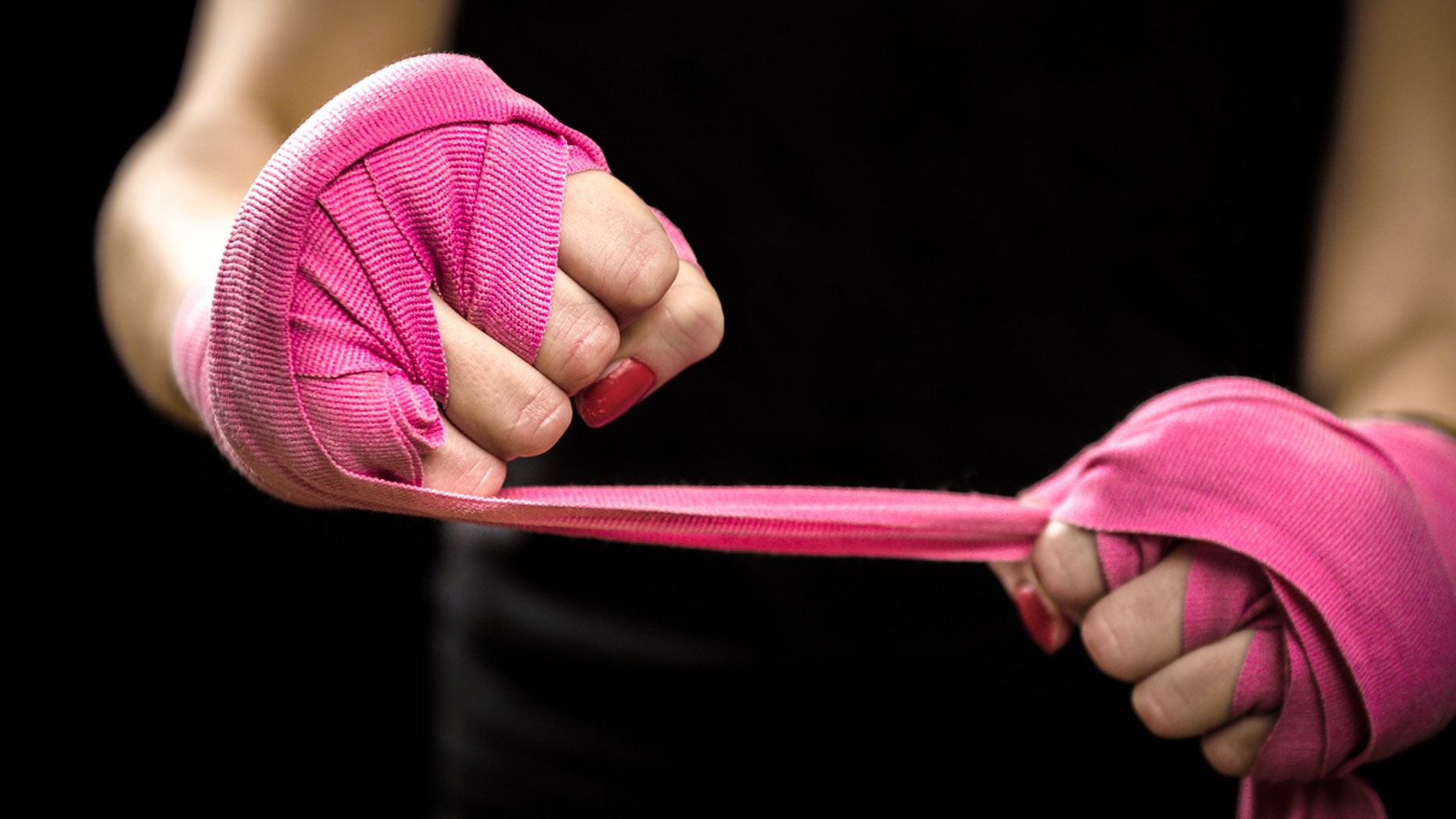 Woman is wrapping hands with pink boxing wraps. Isolated on black with red nails. Strong hand and fist, ready for fight and active exercise