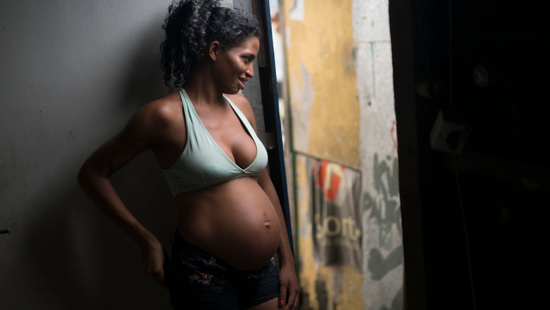 In this Jan. 29, 2016 photo, Tainara Lourenco smiles as she chats with neighbors from the entrance of home at a slum in Recife, Brazil. Unemployed and five months pregnant, 21-year-old Lourenco lives in a slum at the epicenter of Brazils tandem Zika and microcephaly outbreaks, the state of Pernambuco. (AP Photo/Felipe Dana)