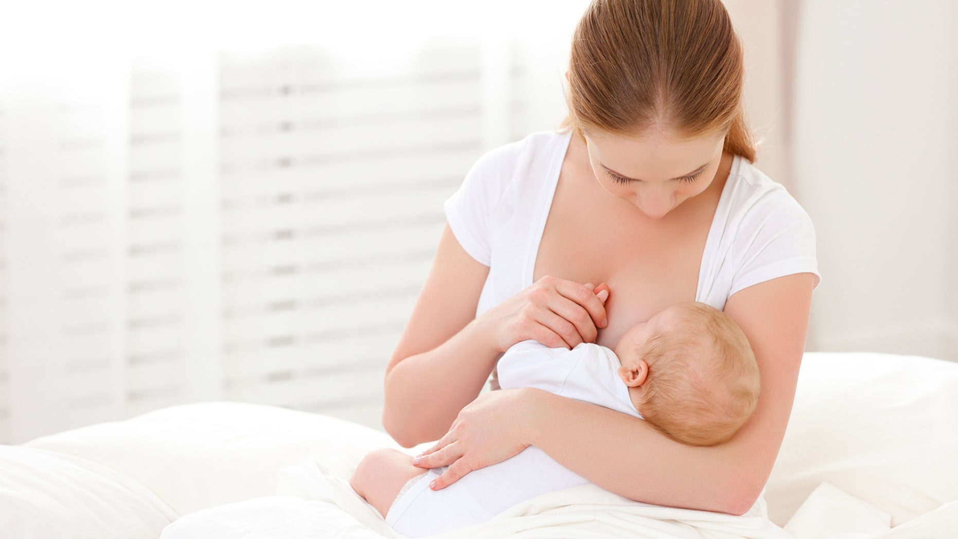 mother breastfeeding her newborn baby in a white bed