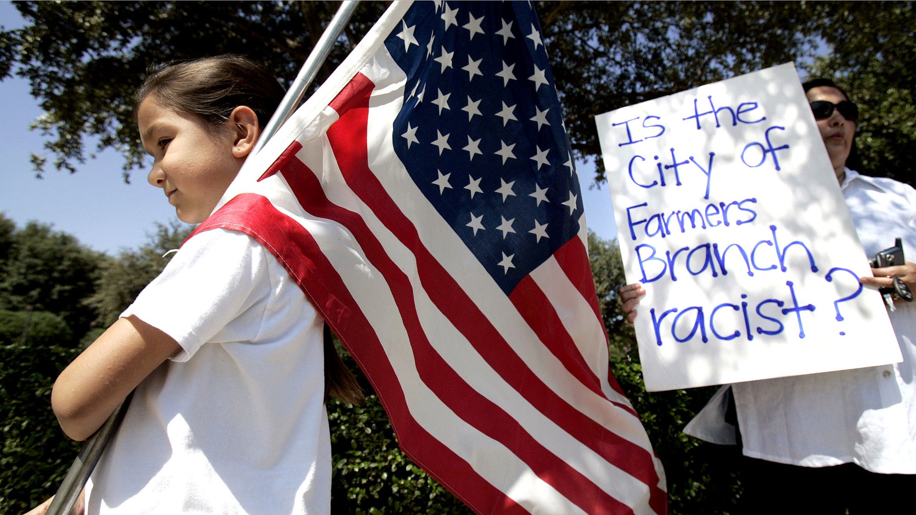 In this Aug. 26, 2006 file photo, Natalie Villafranca, 6, left, hold a flag as her mother, Elizabeth Villafranca, holds a sign in front of city hall in Farmers Branch, Texas, during an immigration law protest. (AP Photo/L.M. Otero, File)