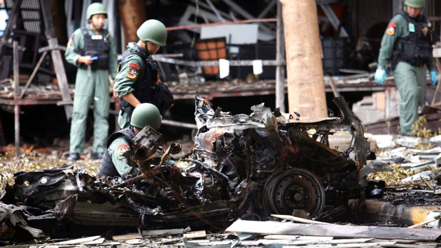 Thai bomb squad officers examine the wreckage of a car.