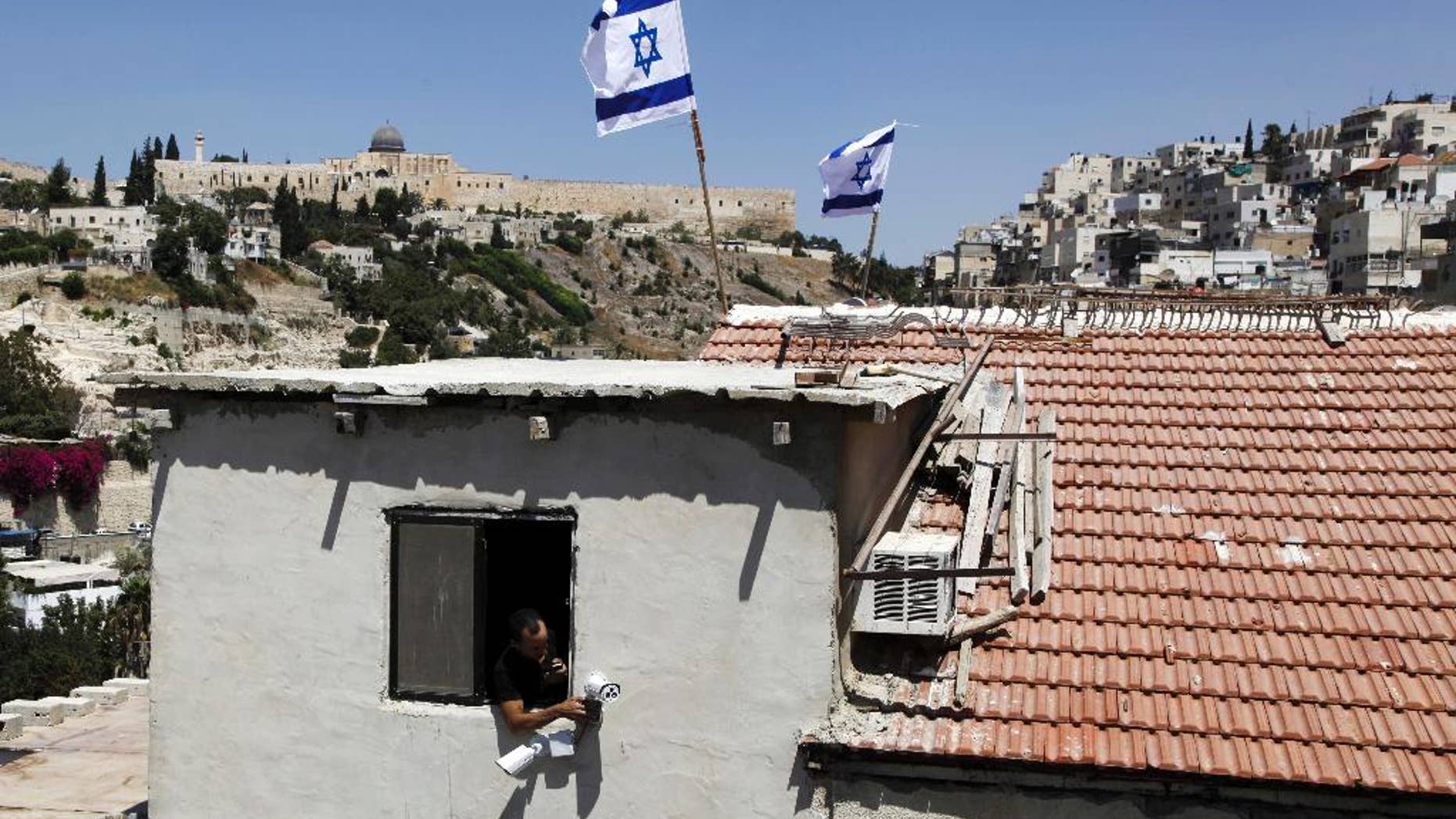 A man is seen from a window as Israeli flags fly on top of a house in Silwan neighborhood of east Jerusalem Thursday, Aug. 27, 2015. Ultra-nationalist Israelis have taken over the building in the heart of an Arab neighborhood in east Jerusalem, raising fears of fresh violence in the tense area. A small group of activists from the Ateret Cohanim settler organization moved into the building on Thursday. It was the latest in a wave of settler advances since nationalist Jews began buying up properties in Palestinian neighborhoods two decades ago. (AP Photo/Mahmoud Illean)