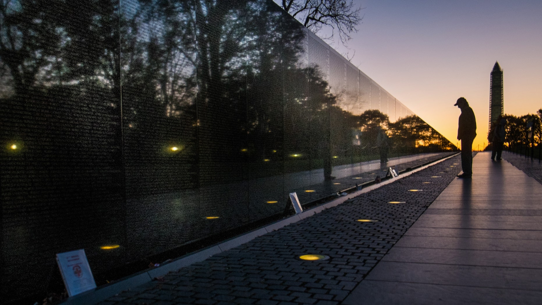 A visitor at the Vietnam War Memorial in Washington passes early in the morning on Veterans Day, Monday, Nov. 11, 2013, to look at the names inscribed on the wall. Several ceremonies are scheduled in the Nation's Capitol to honor those who have served in the U.S. military including a wreath laying at Vietnam War Memorial. The Washington Monument is at right. (AP Photo/J. David Ake)