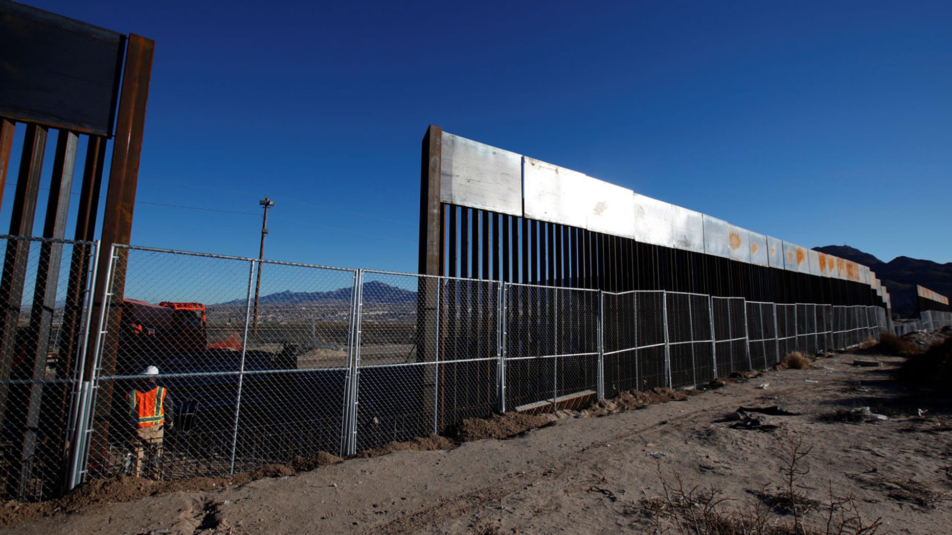 FILE: A worker stands next to a newly built section of the U.S.-Mexico border fence at Sunland Park, Calif.
