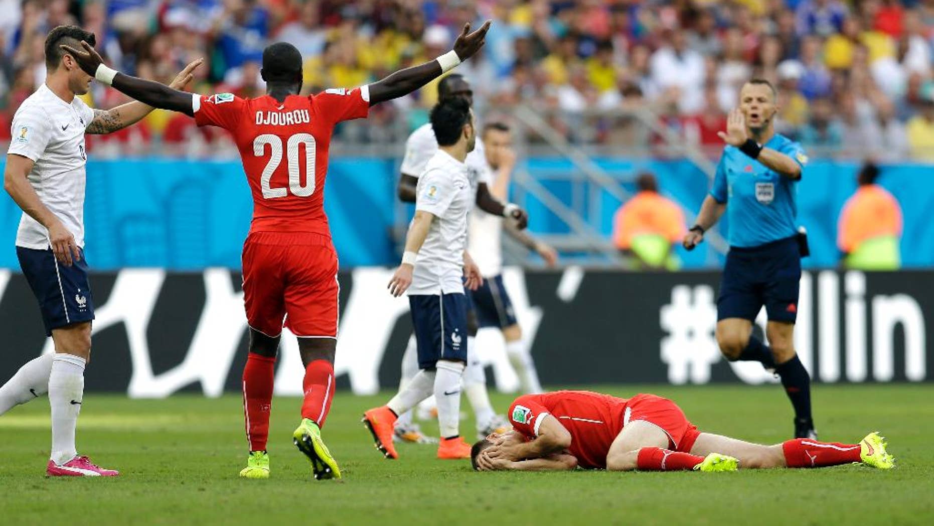 Switzerland's Johan Djourou (20) signals to referee Sander Van Roekel, of the Netherlands, as Steve von Bergen lies on the ground after getting hit by France's Olivier Giroud during the group E World Cup soccer match between Switzerland and France at the Arena Fonte Nova in Salvador, Brazil, Friday, June 20, 2014. (AP Photo/Natacha Pisarenko)