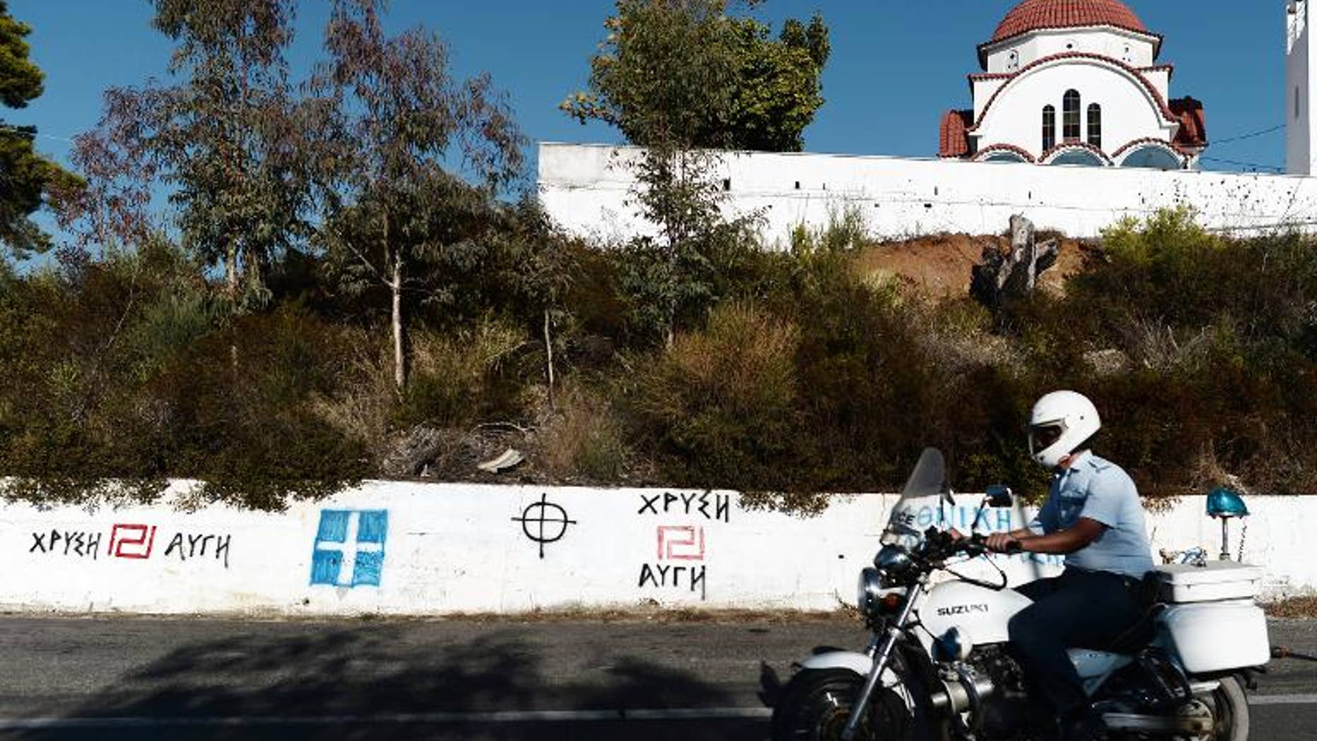 A policeman rides his motorcycle in front of Golden Dawn and nationalist graffiti in southern Greece, on September 29, 2013. Greek police swooped on the neo-Nazi Golden Dawn party, arresting its leadership and hunting for dozens of members across the country in a crackdown sparked by the murder of a leftist musician. AFP PHOTO / ARIS MESSINIS