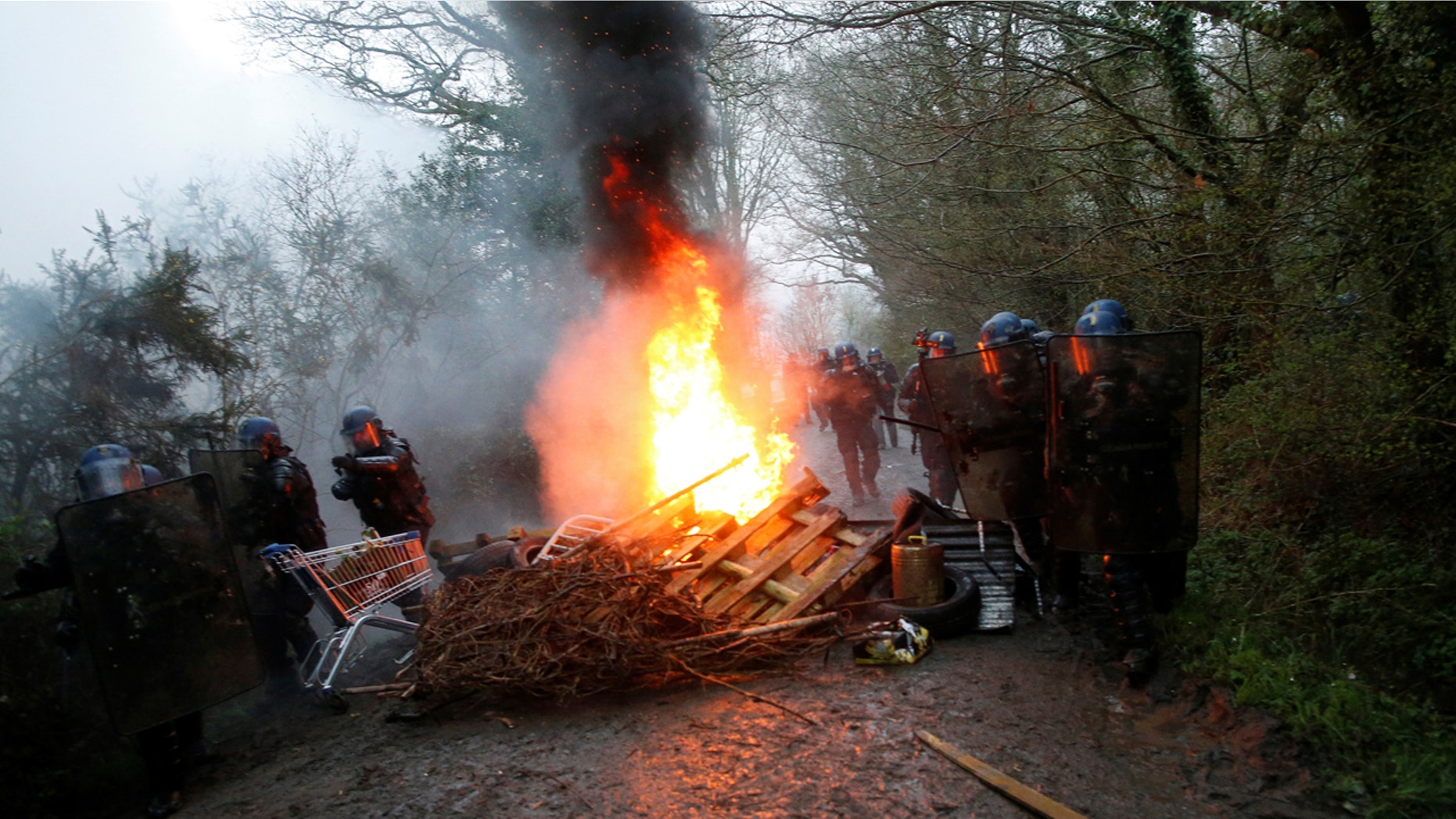 French gendarmes stand near burning debris on a road during an evacuation operation in Notre-Dame-des-Landes, near Nantes, France.