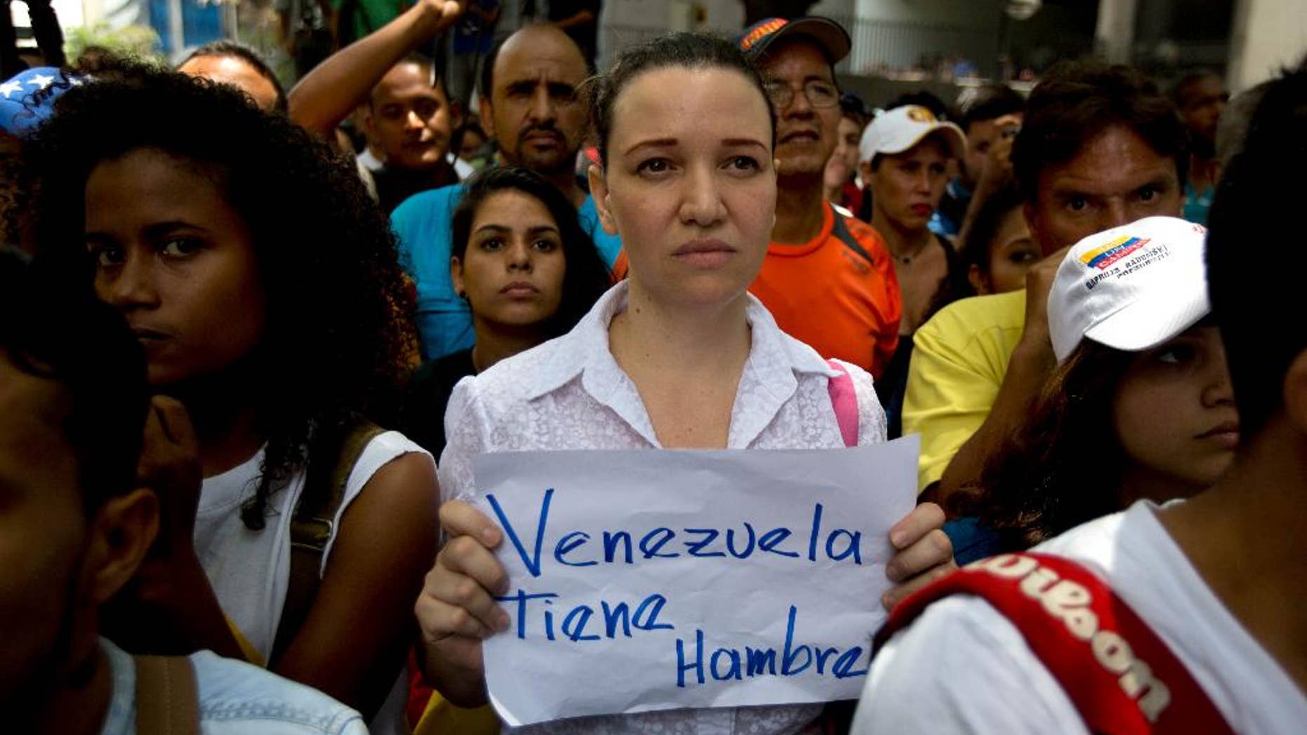 An opposition members holds a handwritten message that that reads in Spanish; "Venezuela is hungry," during a protest outside the court offices of the Chacao municipality, in Caracas, Venezuela, Wednesday, May 25, 2016. Opposition members held a demonstration to demand authorities hold a recall referendum on cutting short Nicolas Maduro's presidency. (AP Photo/Fernando Llano)