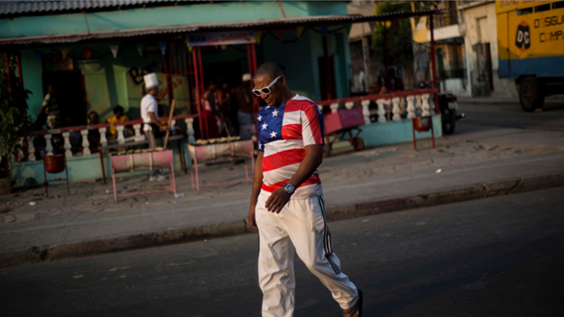 In this March 21, 2015 photo, a man wears a shirt with a U.S. flag design in Santiago, Cuba. Its easier to get from Havana to Miami than to the islands second-largest city, which has just two overbooked flights a day and trains that are achingly slow and unpredictable. (AP Photo/Ramon Espinosa)