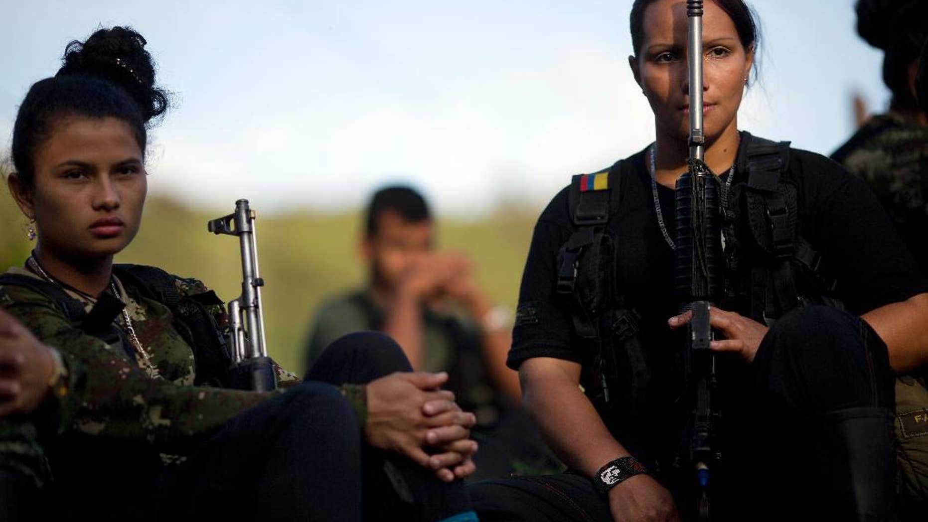 FILE - In this Jan. 4, 2016, file photo, Juliana, 20, left, and Mariana, 24, rebel soldiers for the 36th Front of the Revolutionary Armed Forces of Colombia, or FARC, listen to a commander speak on the peace negotiations between the rebels and the Colombian government, in a hidden camp in Antioquia state, in the northwest Andes of Colombia. Colombian President Juan Manuel Santos said Tuesday, June 21, that his government may reach an agreement on a bilateral ceasefire with leftist rebels as early as this week. (AP Photo/Rodrigo Abd,File)