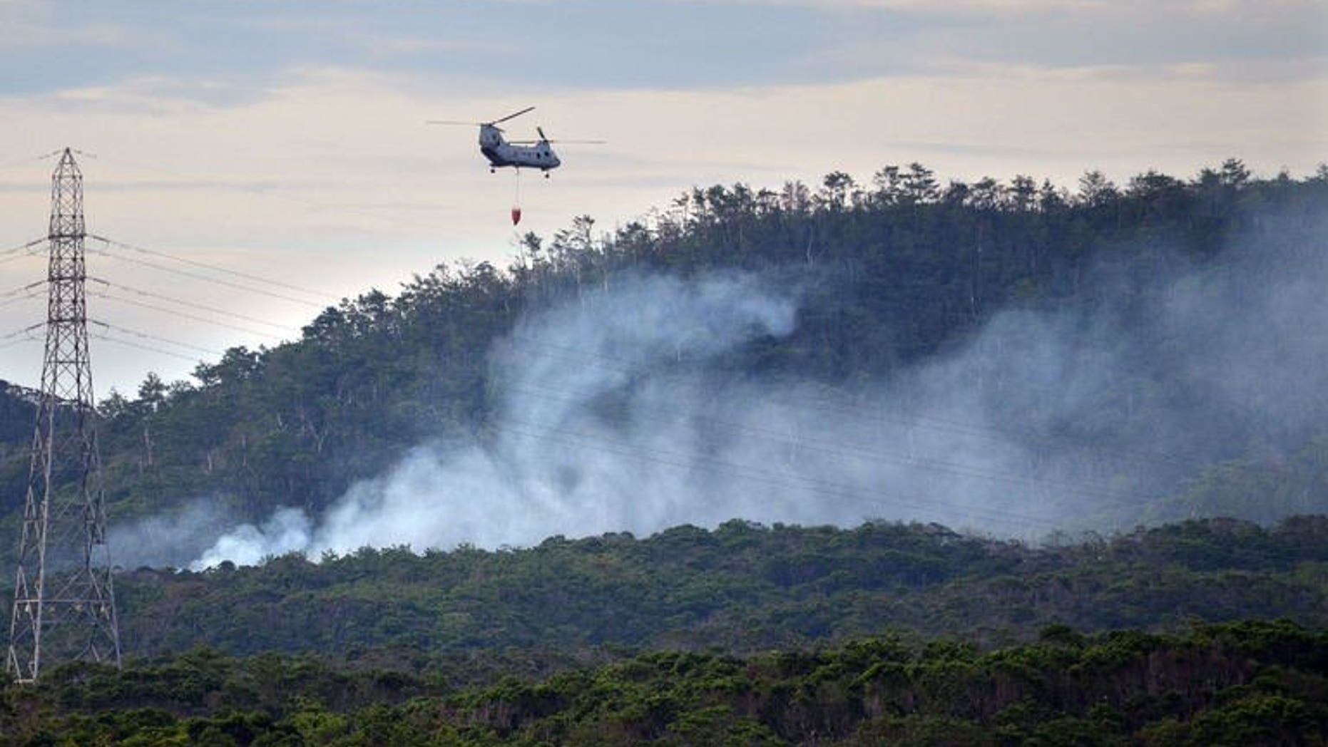A US military helicopter flies on a fire fighting operation after a military helicopter crashed on a mountain on Okinawa island, on August 5, 2013. Japan's prime minister on Tuesday called on the US military to suspend helicopter operations in the country's southern Okinawa island chain after the fatal crash.