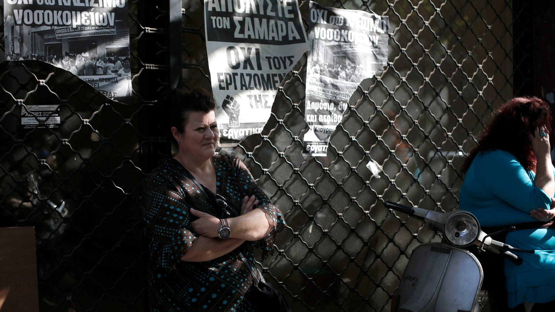 A psychiatric hospital worker stands outside a shuttered shop with posters that read in Greek "No to the hospital closure " and '' Fire (prime minister) Samaras not the workers" during a protest outside the health ministry in central Athens, on Friday, Nov. 1, 2013. About a hundred state health workers took part in the rally to protest planned mandatory public sector employee transfers and suspensions as part of the government's harsh austerity drive. (AP Photo/Petros Giannakouris)