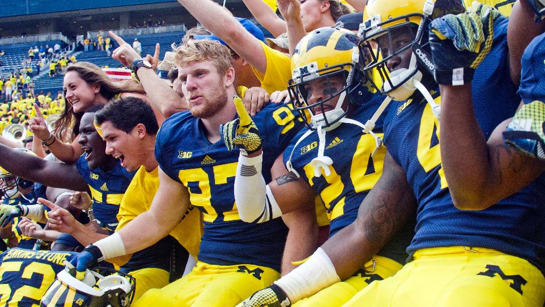 Michigan defensive end Brennen Beyer (97), defensive back Delonte Hollowell (24), and running back De'Veon Smith (4) celebrate in the stands with student fans after beating Appalachian State 52-14 in an NCAA college football game in Ann Arbor, Mich., Saturday, Aug. 30, 2014. (AP Photo/Tony Ding)