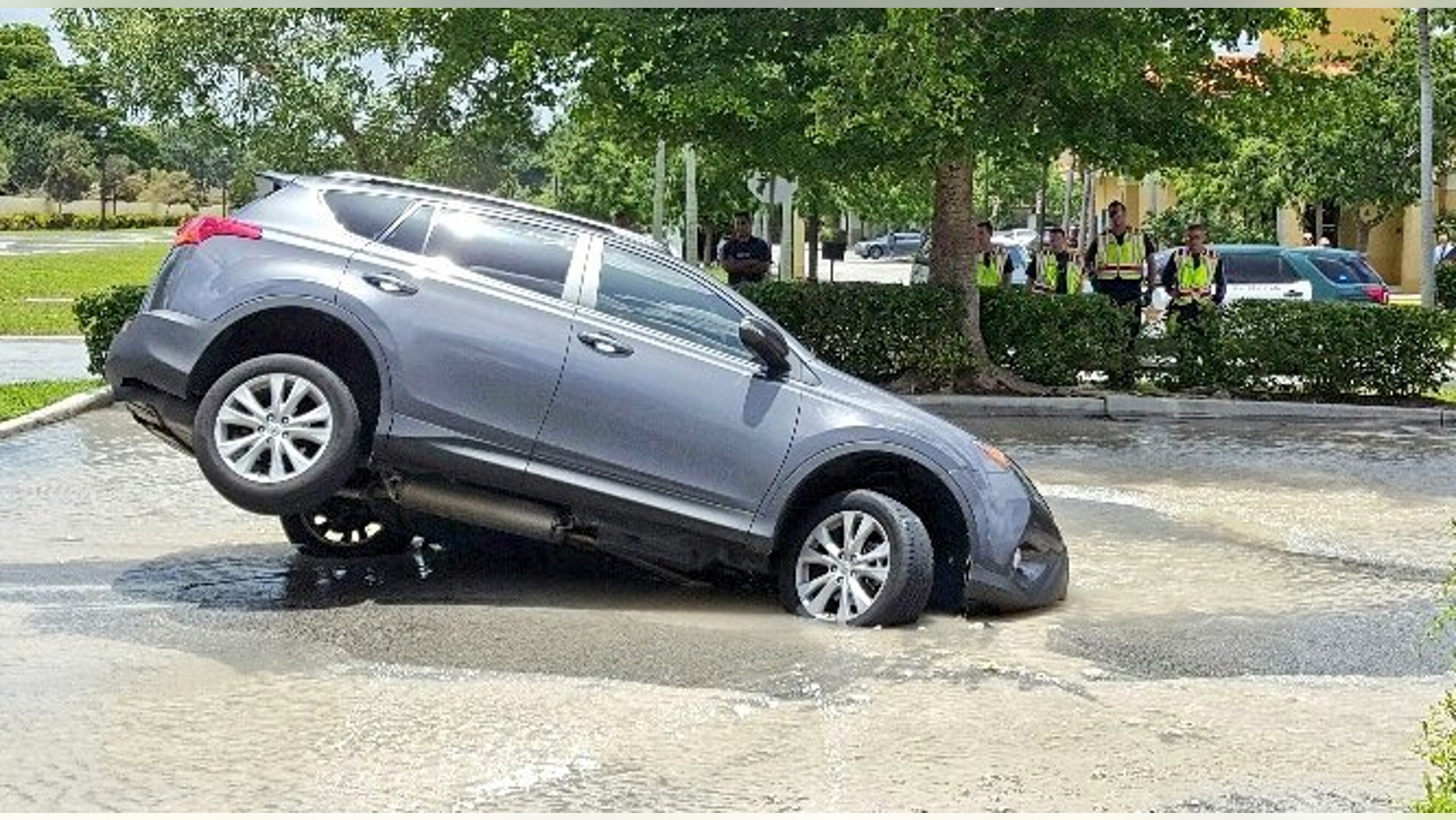 This photo provided by Mike Jachles Broward Sheriff Fire Rescue shows a vehicle partially swallowed by a 10-foot-by-10-foot sinkhole on Thursday, July 7, 2016 in Cooper City, Fla. Dolores Otero drove toward the drive-thru and her car went nose-first into the water. One of the car's back tires was left hanging in the air. Otero and her grandson got safely out of the vehicle, which began to fill with water. (Mike Jachles/Broward Sheriff Fire Rescue via AP)
