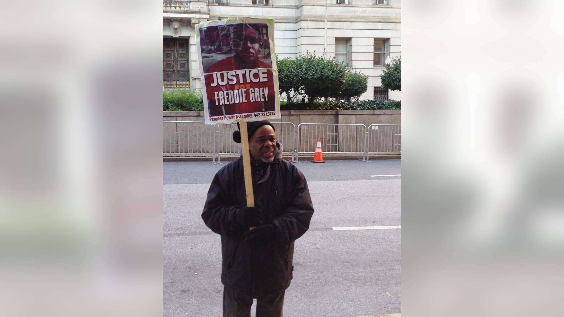 Demonstrator Arthur Johnson carries a sign advocating justice for Freddie Gray on Monday, Dec. 7, 2015, outside the courthouse in Baltimore where the trial of Offcer William Porter enters its second week. (AP Photo/David Dishneau)