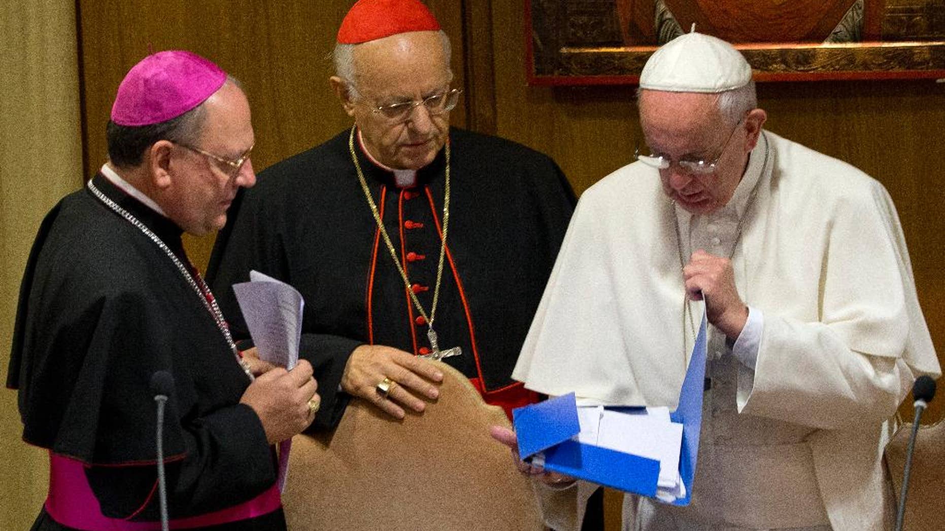 Pope Francis, right, checks a folder next to Bishop Fabio Fabene, left, and Cardinal Lorenzo Baldisseri as they arrive at a morning session of the two week-long Synod of bishops, at the Vatican, Tuesday, Oct. 6, 2015. (AP Photo/Alessandra Tarantino)