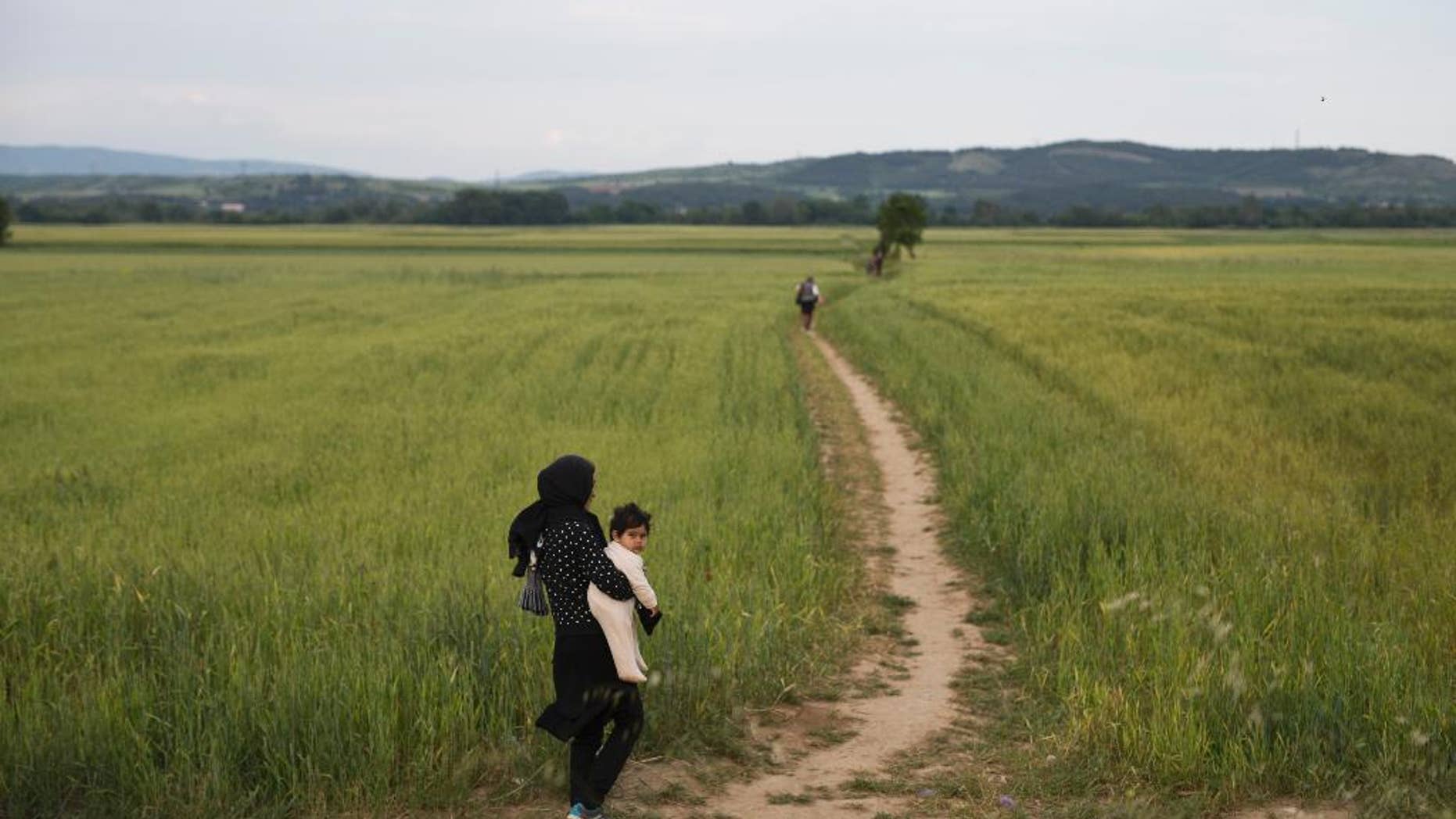 A woman walk with her baby on fields as a group of refugees and migrants leave the northern Greek border point of Idomeni, Greece, on Tuesday May 10, 2016. About 54,000 refugees and migrants are currently stranded in Greece as 10,000 are camped in Idomeni, after the European Union and Turkey reached a deal designed to stem the flow of refugees into Europe’s prosperous heartland. (AP Photo/Petros Giannakouris)
