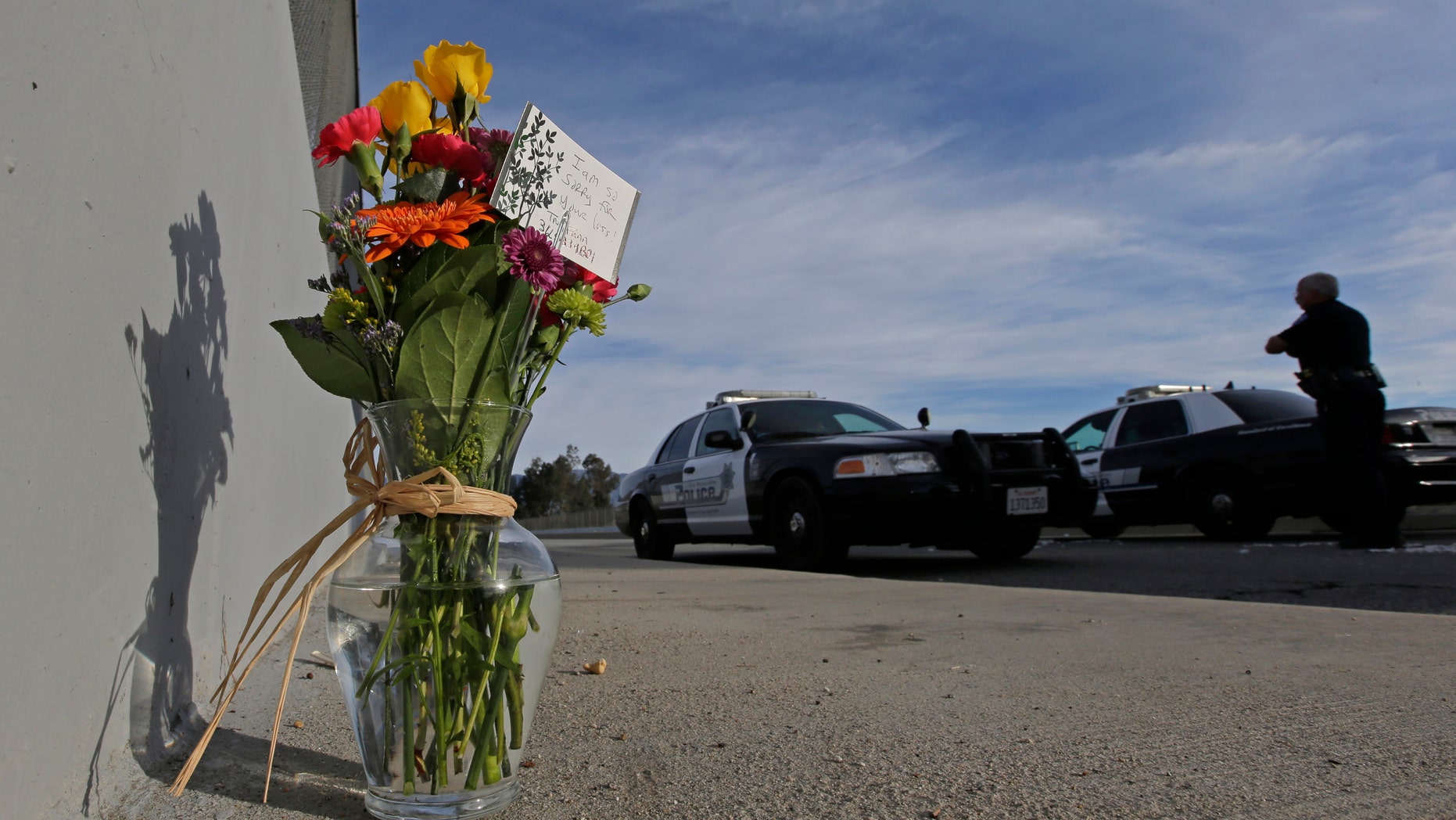 Flowers are left by the side of the road as a San Bernardino police officer blocks the road leading to the site of yesterday's mass shooting on Thursday, Dec. 3, 2015 in San Bernardino, Calif. A heavily armed man and woman dressed for battle opened fire on a holiday banquet for his co-workers Wednesday, killing multiple people and seriously wounding others in a precision assault, authorities said. Hours later, they died in a shootout with police. (AP Photo/Chris Carlson)