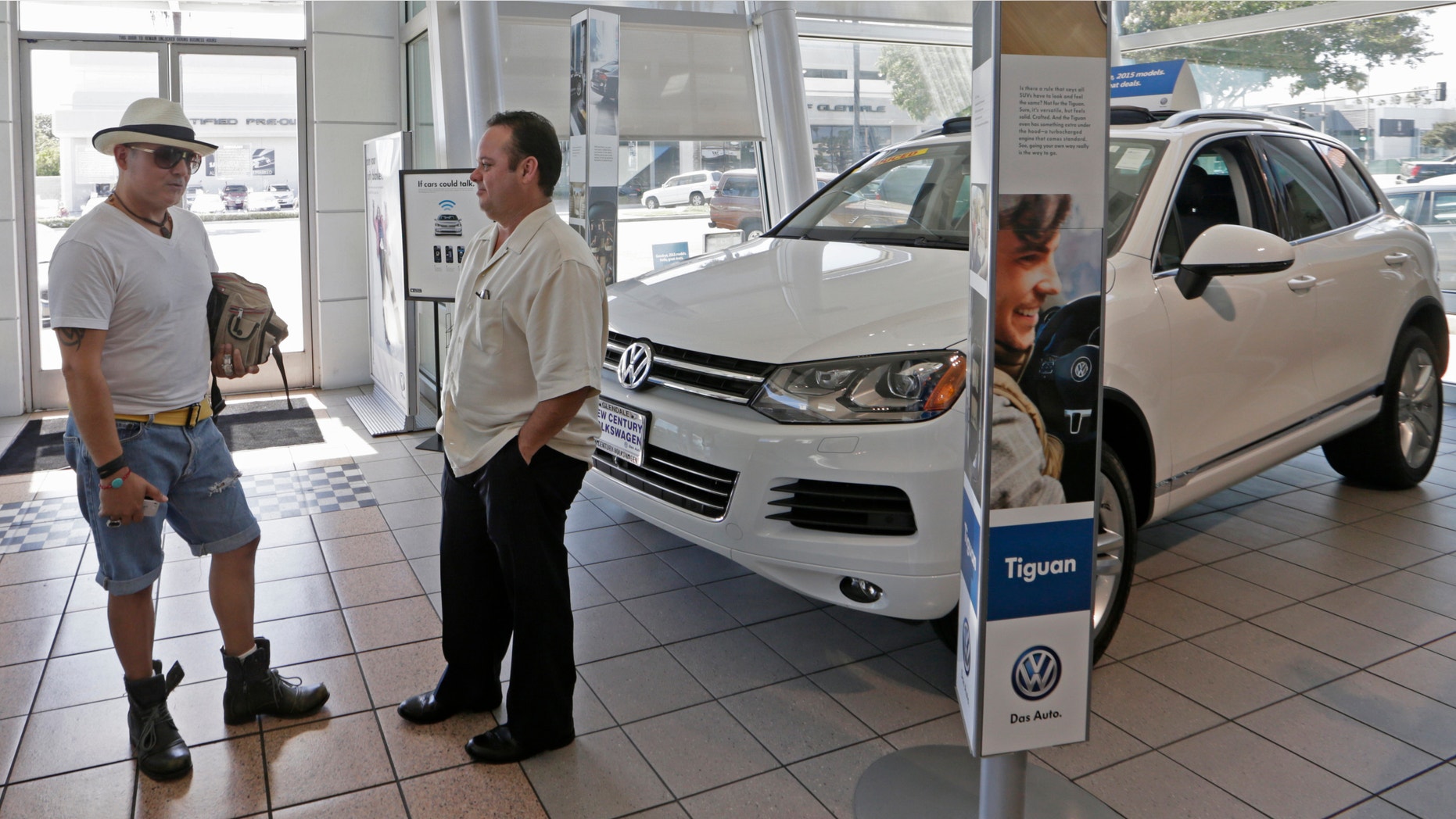 In this Thursday, July 2, 2015, photo, customer Armando Barillas, originally from Guatemala, left, talks to Sergio Rosas, sales manager at the New Century Volkswagen dealership in Glendale, Calif. At least 31 models are being redesigned for 2016, including big names like the Volkswagen Passat and the Toyota Prius, according to the car buying site Edmunds.com. So, dealers are slashing thousands of dollars off the cost of 2015 models to clear them off their lots. (AP Photo/Damian Dovarganes)