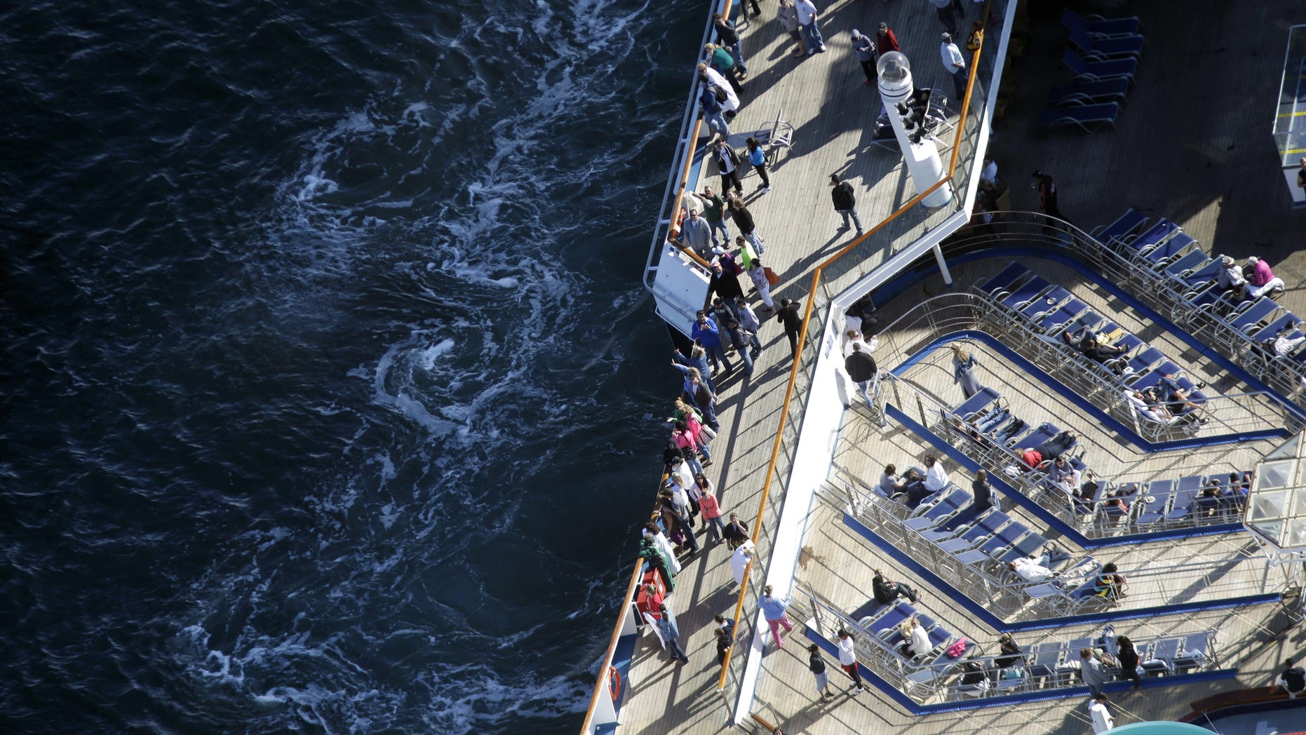 Passengers stand on the upper deck of the disabled Carnival Lines cruise ship Triumph as it is towed to harbor off Mobile Bay, Ala., Thursday, Feb. 14, 2013. The ship with over 1,000 passengers aboard has been idled for nearly a week in the Gulf of Mexico following an engine room fire. (AP Photo/Gerald Herbert)