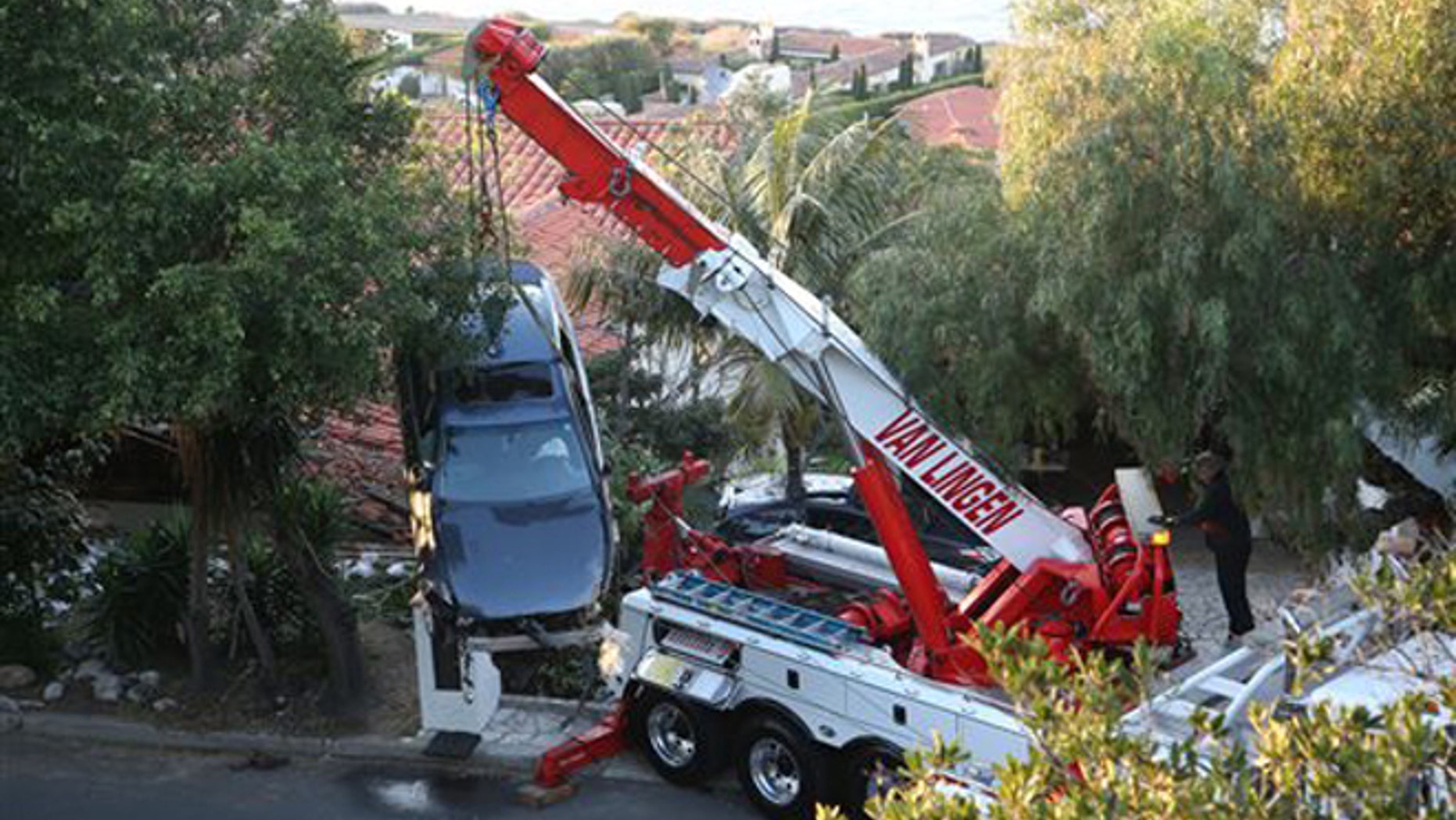 A crane removes a car that crashed off Palos Verdes Drive west and ended up on the roof of a home in Palos Verdes Estates, Calif. Wednesday, Feb. 3, 2016. Firefighters pulled the man from the damaged car and took him to a hospital, but he wasnt seriously hurt, and no one else was injured. (Chuck Bennett/Daily Breeze via AP)