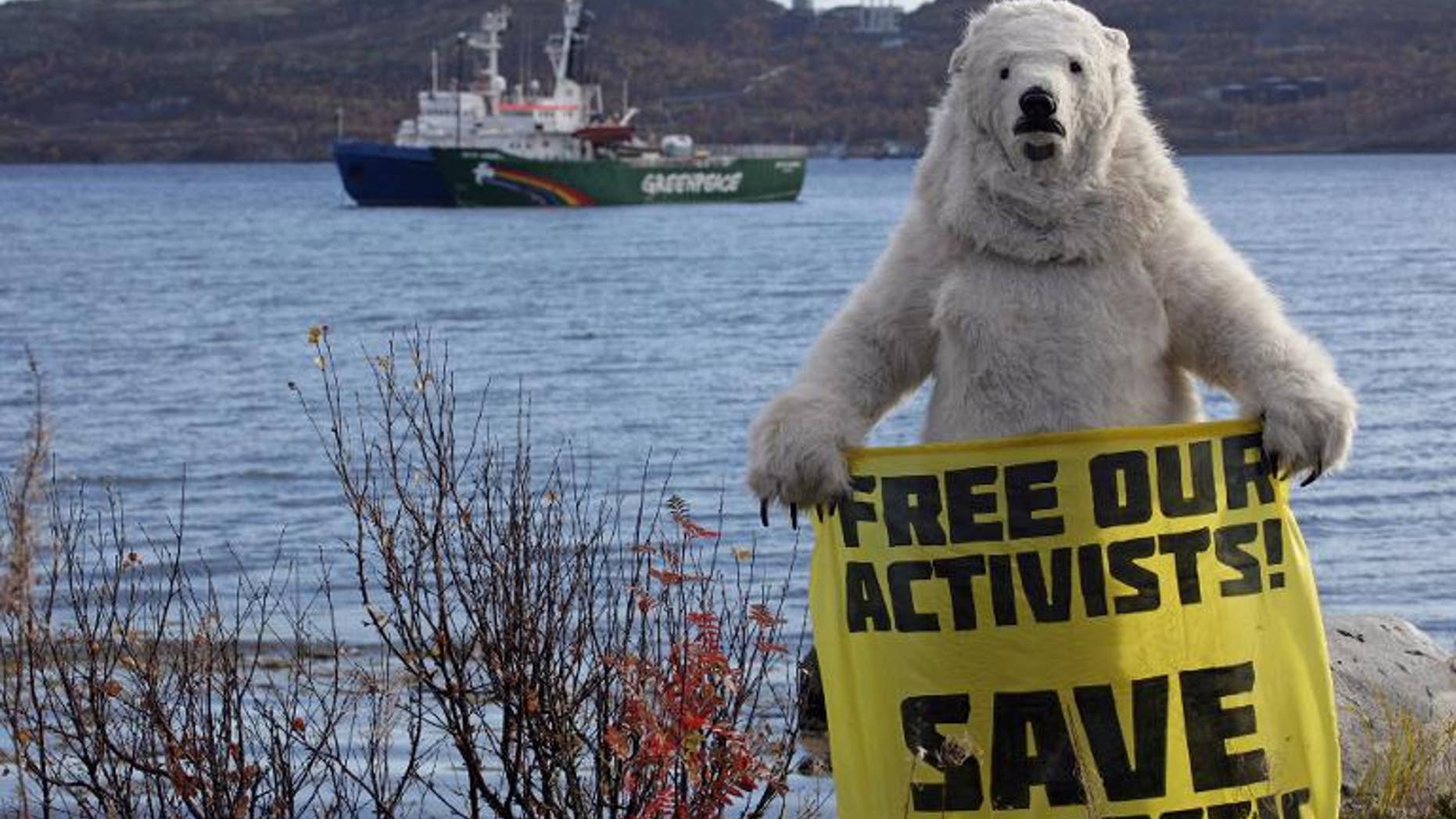 An activist dressed as a polar bear holds a banner in front of Greenpeace's Arctic protest ship, moored beside a Russian Coast Guard ship in Kola Bay near Murmansk on September 24, 2013, in a photo provided by Greenpeace International
