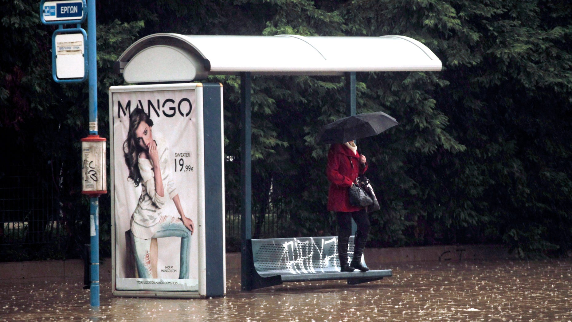 A woman shelters from the rain and the flodding at a bus stop, by standing on a bench, on a flooded highway linking Athens with its port of Piraeus, during a rainstorm on Friday, Feb. 22, 2013. Hours of heavy rainfall in Athens caused extensive flooding, inundating basements and forcing authorities to close major roads and a central subway station. The Greek fire brigade says it received more than 900 calls to pump out water in the greater Athens region Friday. (AP Photo/Petros Giannakouris)
