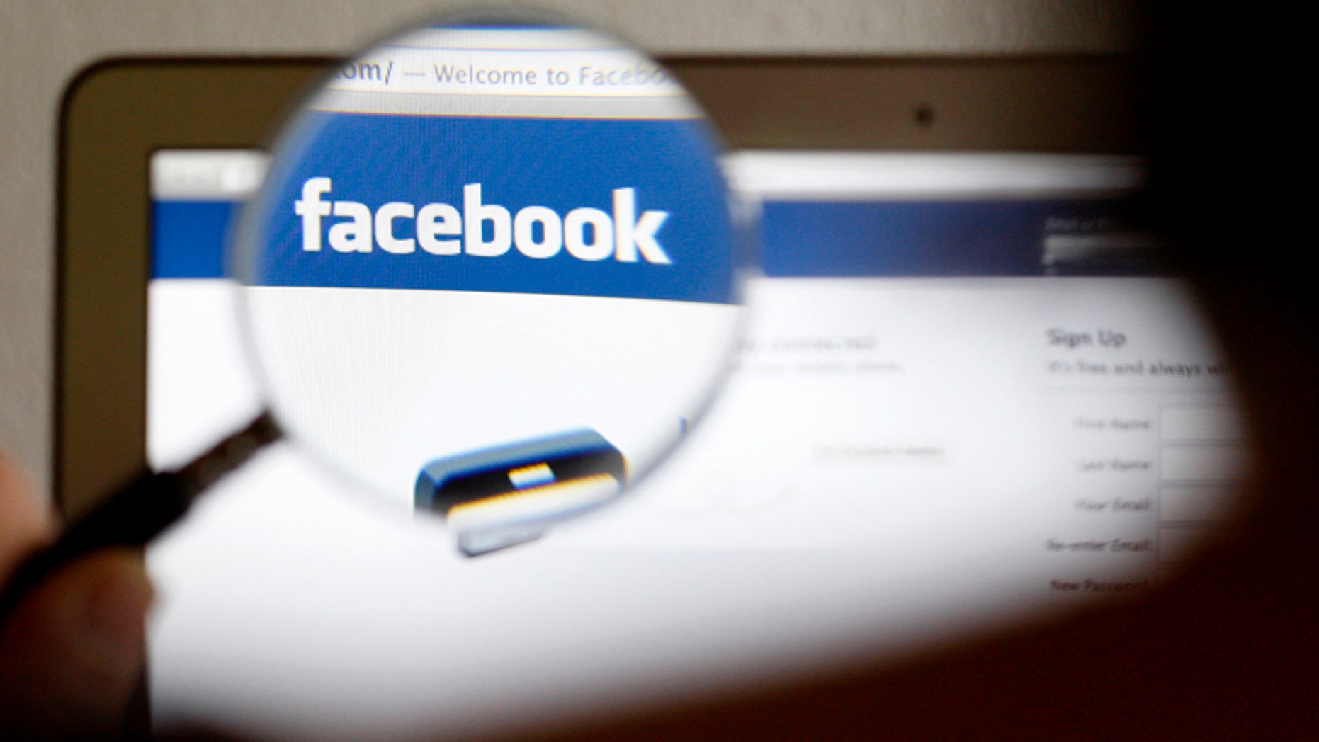 In this photo illustration, a Facebook logo on a computer screen is seen through a magnifying glass.