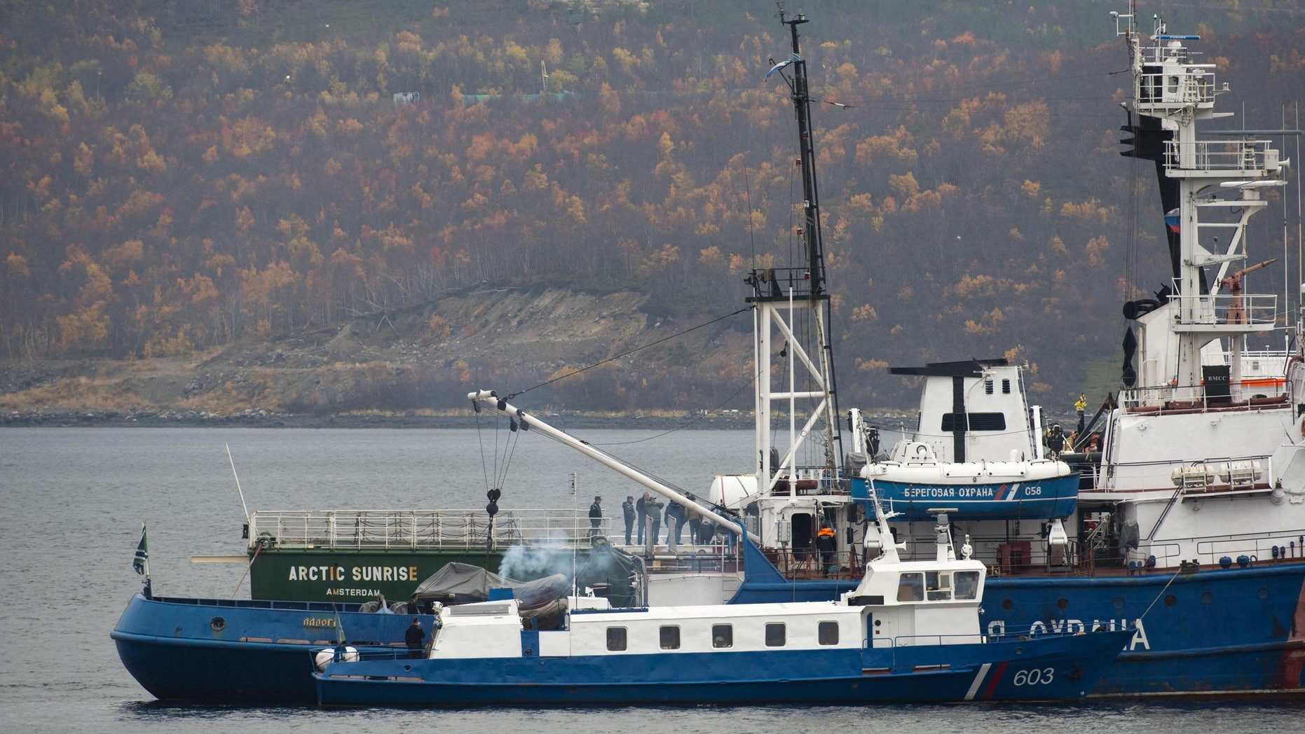 In this photo provided by Greenpeace and taken Wednesday, Oct. 2, 2013, members of the Russian Investigative Committee accompanied by Peter Willcox, the U.S. captain of the Greenpeace ship Arctic Sunrise inspect the vessel, in back, near Murmansk, Russia. Russian investigators have charged the entire 30-member crew of a Greenpeace ship with piracy for a protest at a Russian oil platform in the Arctic. (AP Photo/Greenpeace, Dmitri Sharomov)