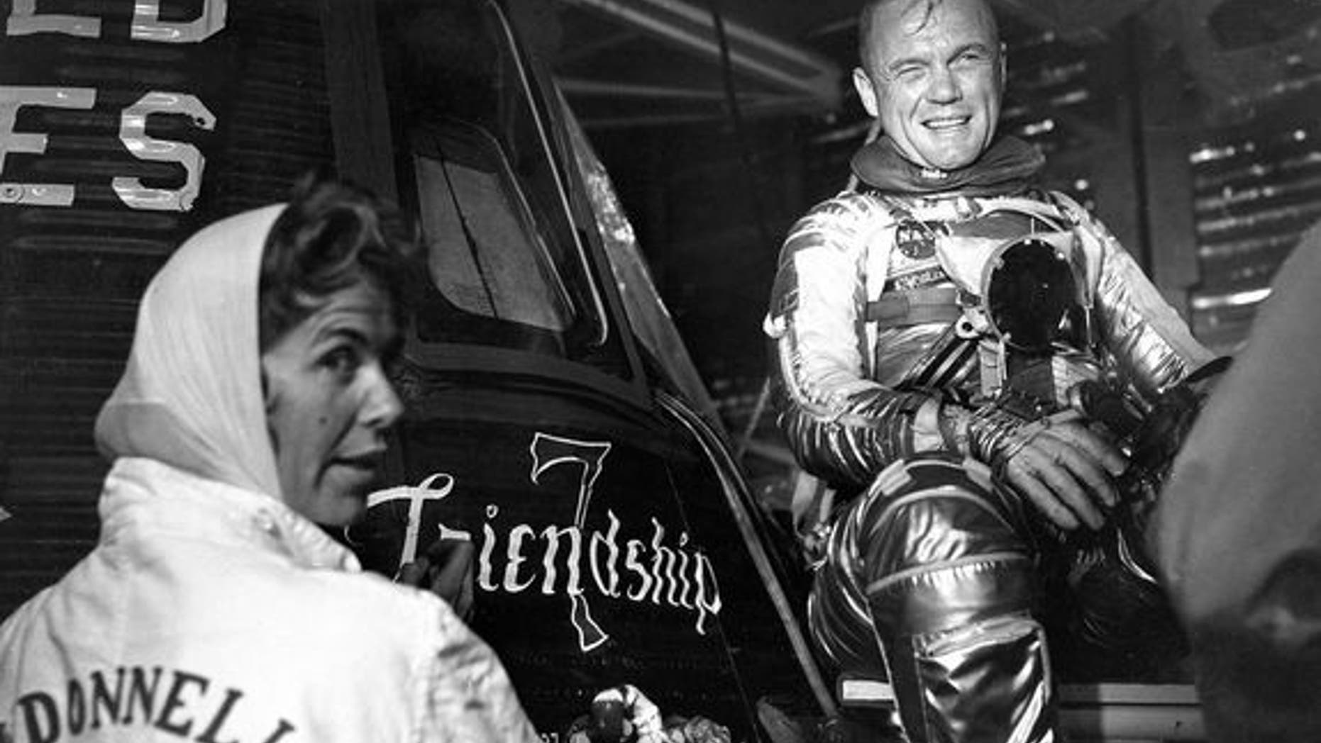 Artist Cece Bibby (at left) puts the final touches on the Friendship 7 logo as astronaut John Glenn looks on in approval.