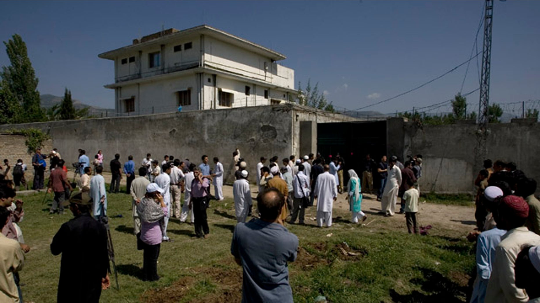 Local people and media gather outside the perimeter wall and sealed gate into the compound and a house where al-Qaida leader Osama bin Laden was caught and killed late Monday, in Abbottabad, Pakistan, on Tuesday, May 3, 2011. Local residents showed off small parts of what appeared to be a U.S. helicopter that Washington said malfunctioned and was disabled by the American commando strike team as they retreated, while Pakistan's leader on Tuesday denied suggestions that his country's security forces had sheltered Osama bin Laden. (AP Photo/Anjum Naveed)