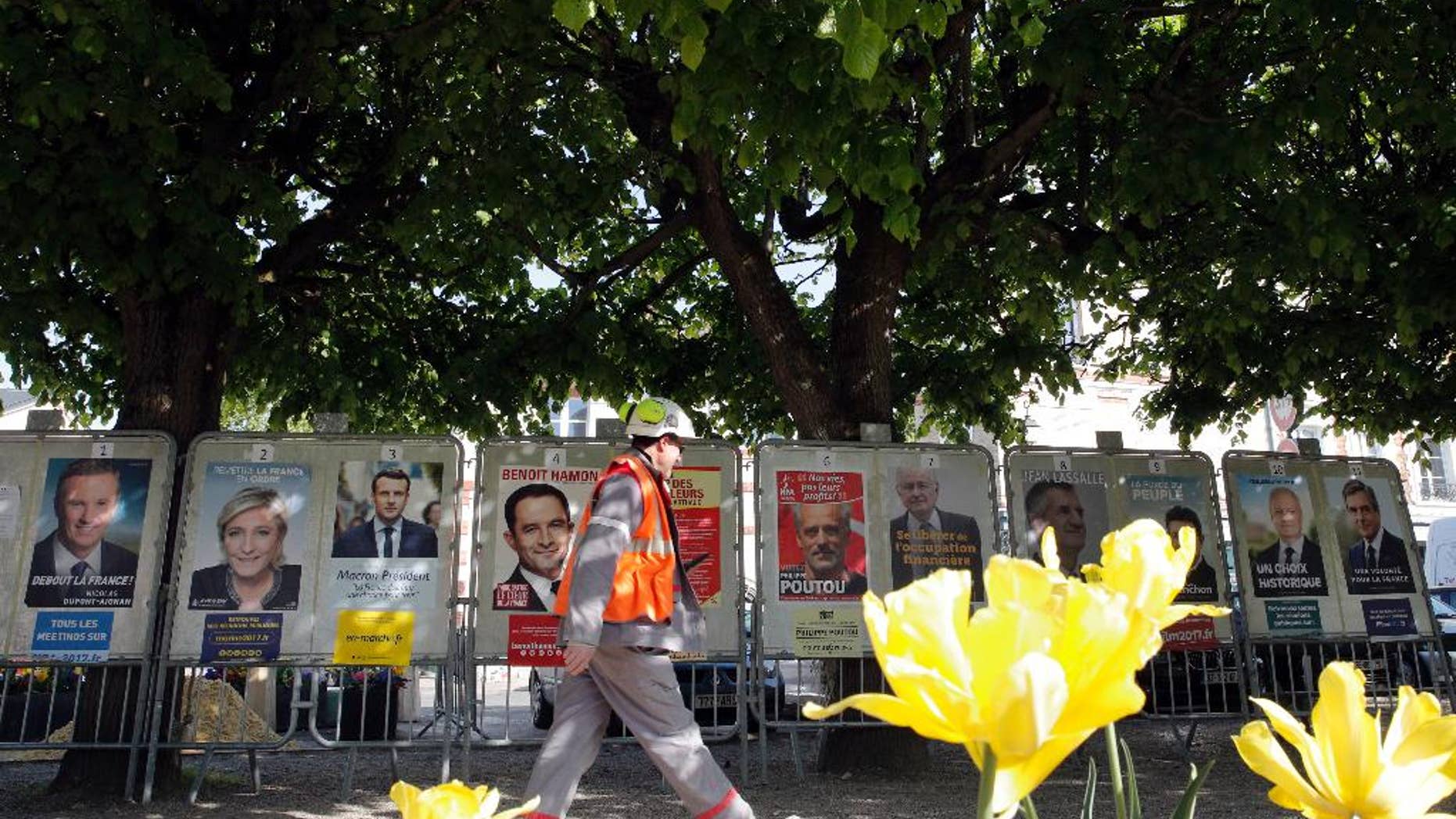 A man walks past French presidential campaign posters displayed in Marnes-la-Coquette, outside Paris, Thursday, April 20, 2017. The two-round presidential election is set for April 23 and May 7. (AP Photo/Christophe Ena)