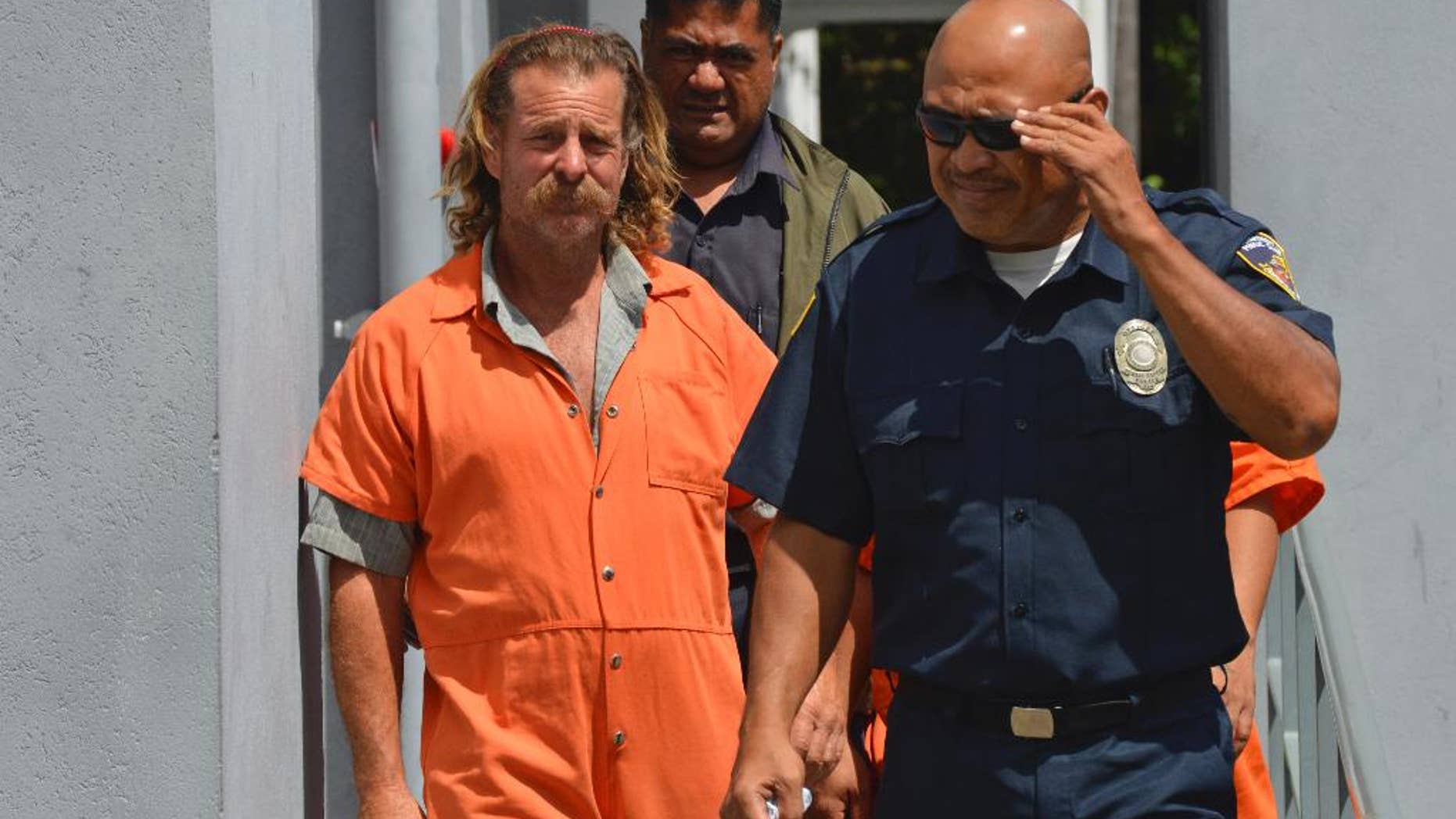 In this Oct. 4, 2016 photo provided by the Samoa News, Dean Fletcher, left, is escorted by a police officer after his initial appearance in the District Court of American Samoa in Pago Pago, American Samoa.