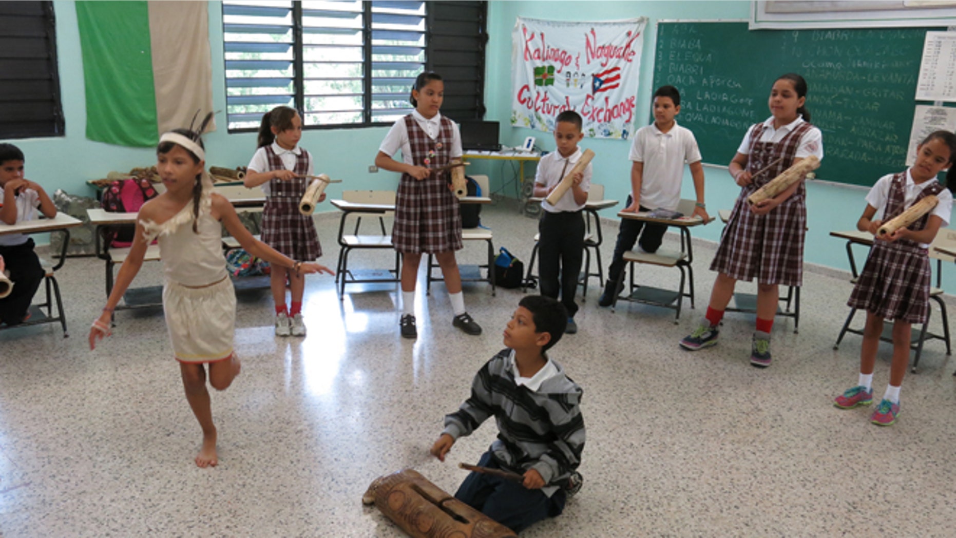In this April 10, 2015 photo, Brayan Lopez, 9, plays a Taino wood drum while students perform a ceremonial dance in San Lorenzo, Puerto Rico. Brayan is a fourth grader and one of the designated caciques - or chieftains - because of his musical skills. He gets to blow a conch shell while other students gather around him and beat on the small, elongated wooden drums. (AP Photo/Danica Coto)