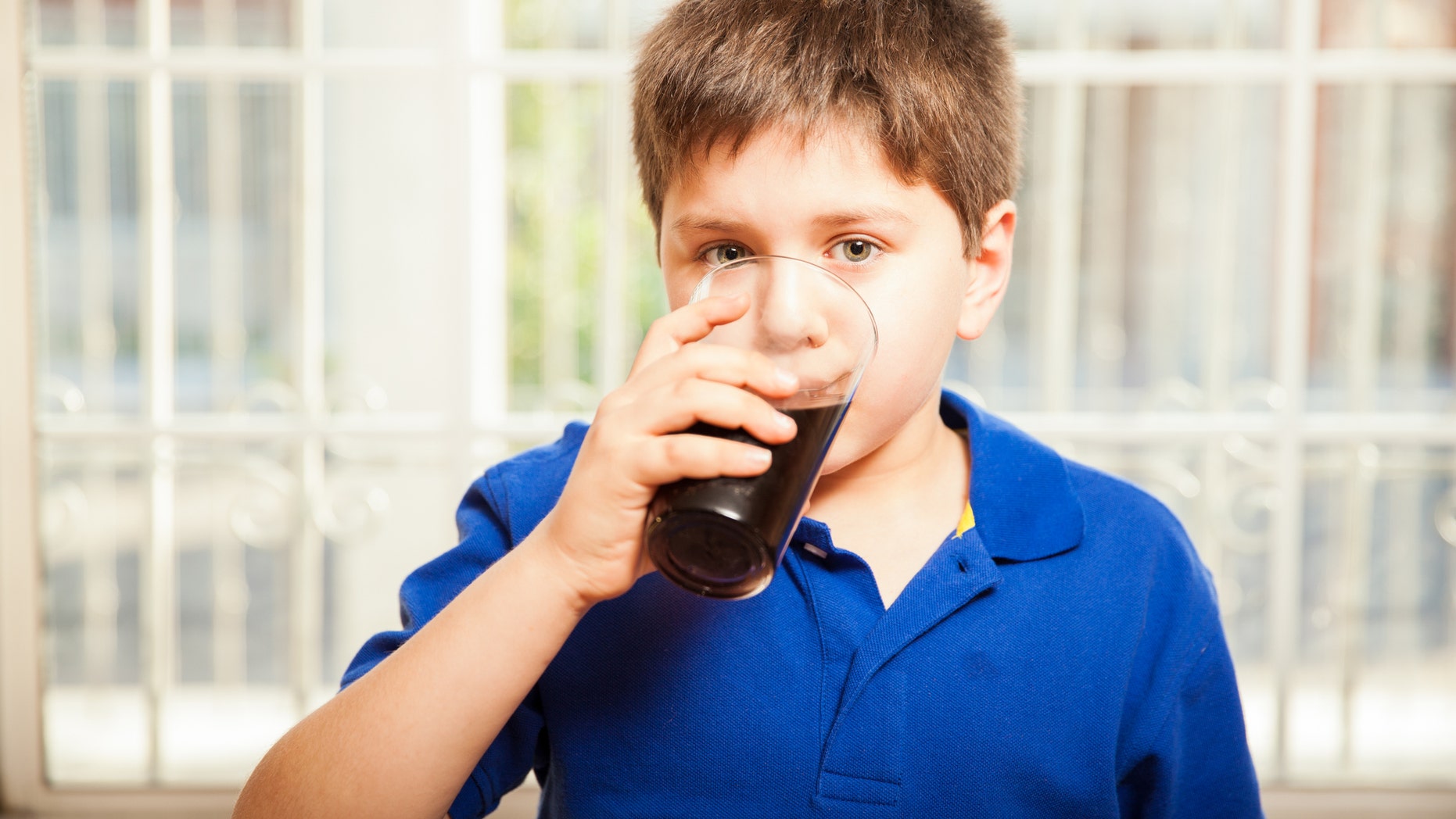 Portrait of a young boy drinking soda from a glass at home