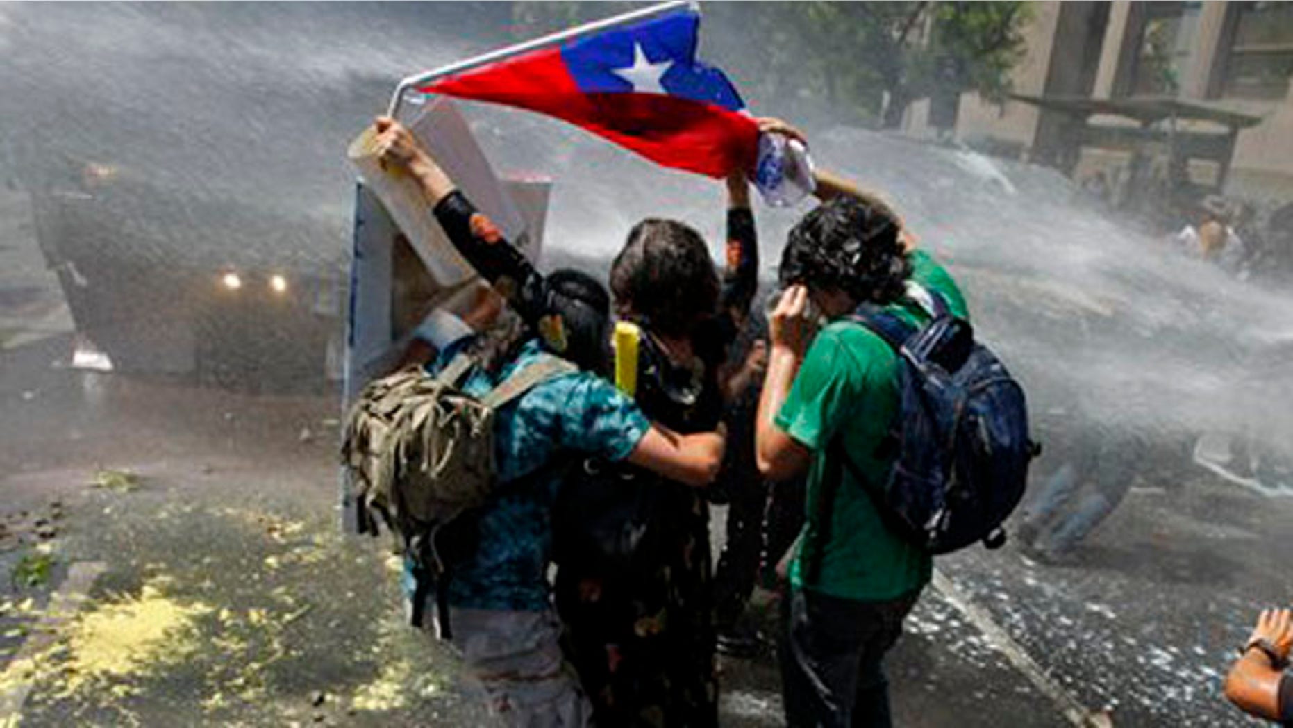 ARCHIVO - En esta foto tomada el 19 de octubre de 2011, un jóven sostiene una bandera chilena mientras la policía trata de dispersar a los estudiantes rociándoles agua en Santiago de Chile. Más de seis meses después de empezar con las protestas que han paralizado a 17 millones de estudiantes del país, los activistas estudiantiles se han ganado el favor popular. Lo que los estudiantes no han conseguido es hacer aprobar las reformas de fondo al sistema educativo, que ellos consideran clave para salvar la educación en Chile.. (AP Foto/Aliosha Marquez, archivo)