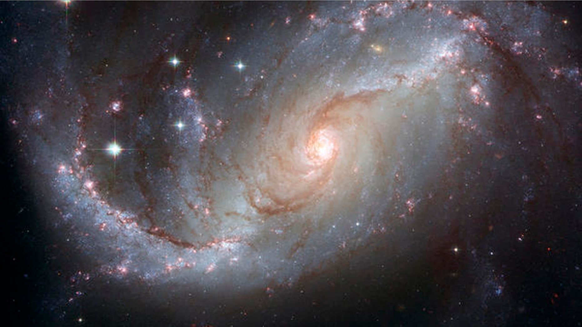 This photo supplied by NASA and the European Space Agency Tuesday, April 3, 2007, is a Hubble Space Telescope view of the barred spiral galaxy NGC 1672, showing up clusters of hot young blue stars along its spiral arms, and clouds of hydrogen gas glowing in red. Delicate curtains of dust partially obscure and redden the light of the stars behind them. NGC 1672s symmetric look is emphasized by the four principal arms, edged by eye-catching dust lanes that extend out from the center. The galaxy, visible from the Southern Hemisphere, is seen almost face on and shows regions of intense star formation. The greatest concentrations of star formation are found in the so-called starburst regions near the ends of the galaxys strong galactic bar. (AP Photo/NASA-ESA) Credit: NASA, ESA