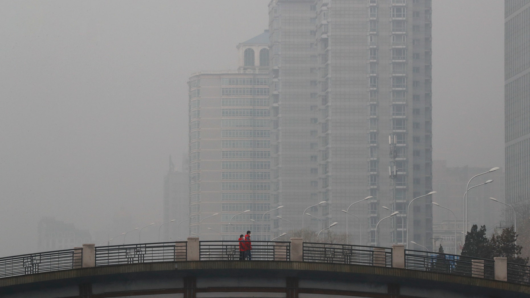 Chinese men wearing masks to filter the pollution walk on a bridge near building shrouded by fog and pollution in Beijing, Thursday, Jan. 5, 2017.