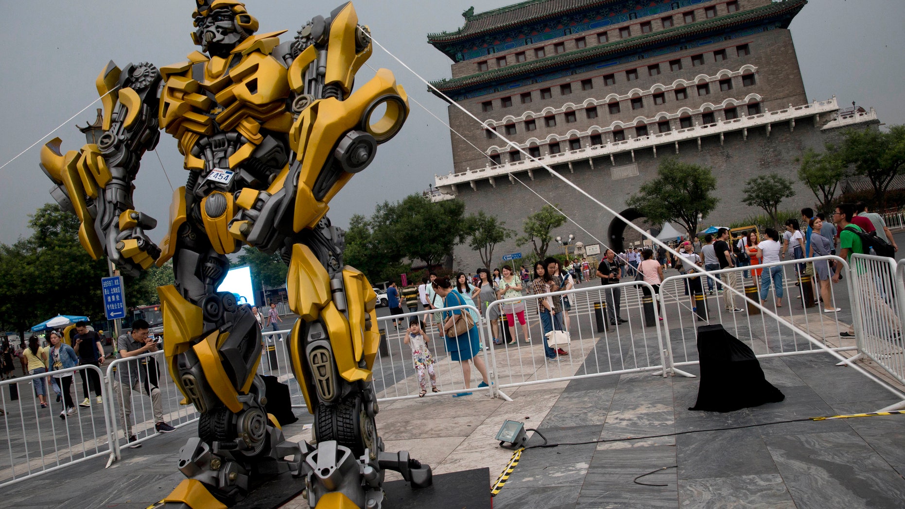 June 21, 2014. A child stands on a barricade fence looks at a replica model of Transformers character Bumblebee on display in front of Qianmen Gate, as part of a promotion of the movie "Transformers: Age of Extinction" in Beijing, China.