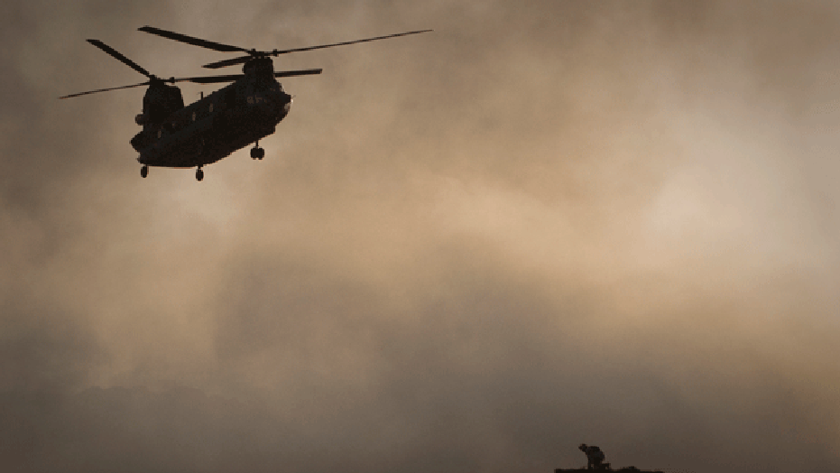A US Marine tries to take cover, perched on a container, trying to shelter from the dust as a Chinook helicopter arrives to pick up supplies at Forward Operating Base Edi in the Helmand Province of southern Afghanistan, in this June 9, 2011 file photo.