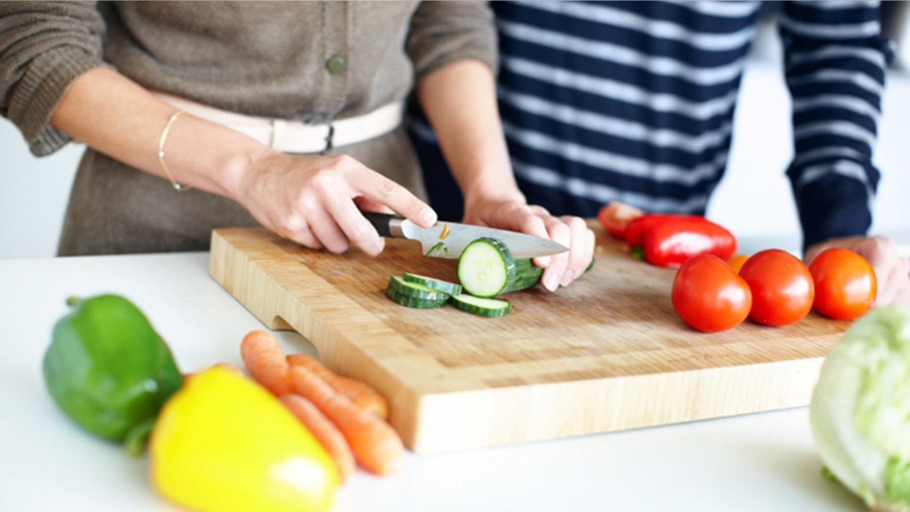 Cropped image of a couple preparing a salad, slicing cucumber on a wooden chopping board